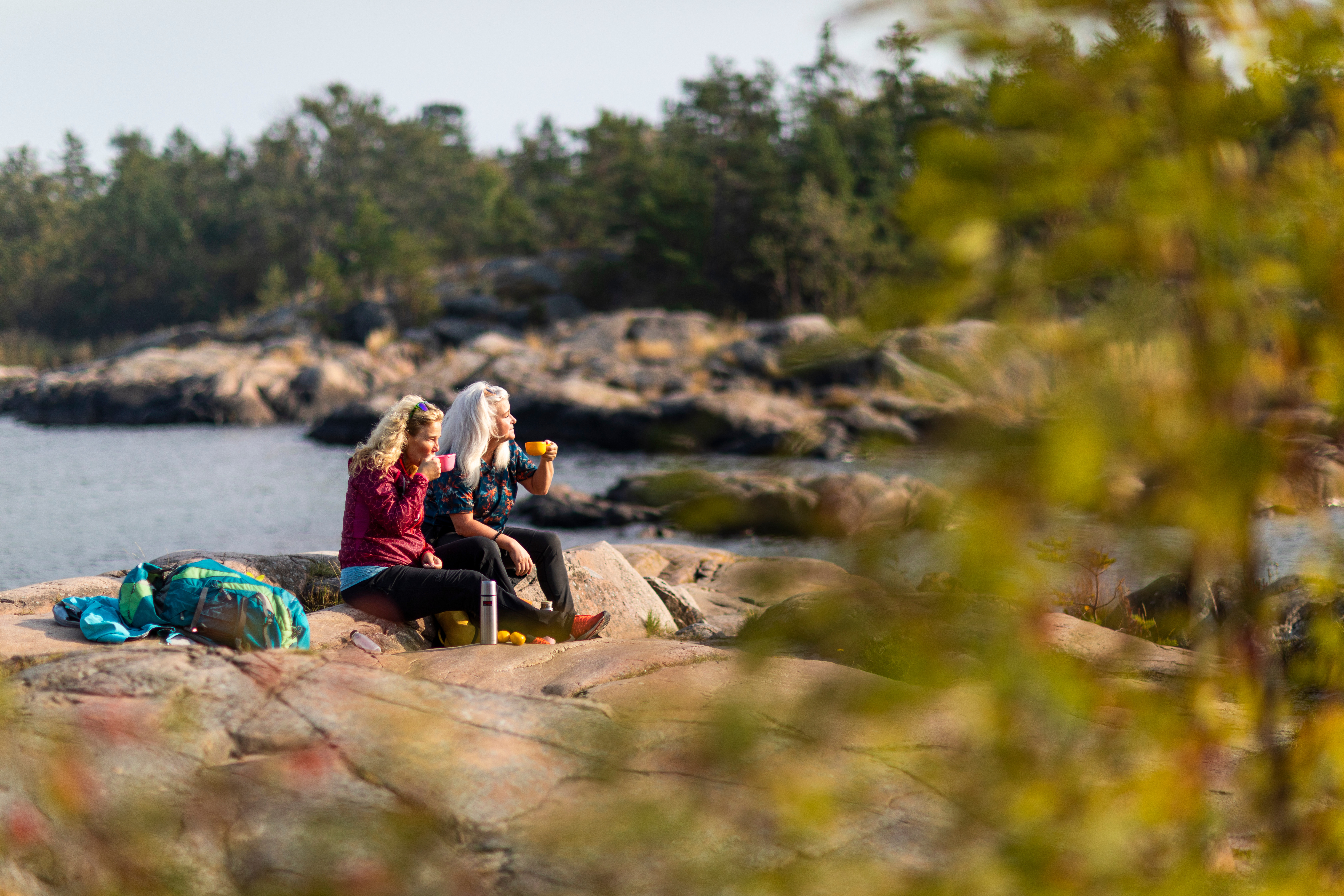 Two women having fika on sunlit coastal rocks along Roslagsleden in the Stockholm archipelago.
