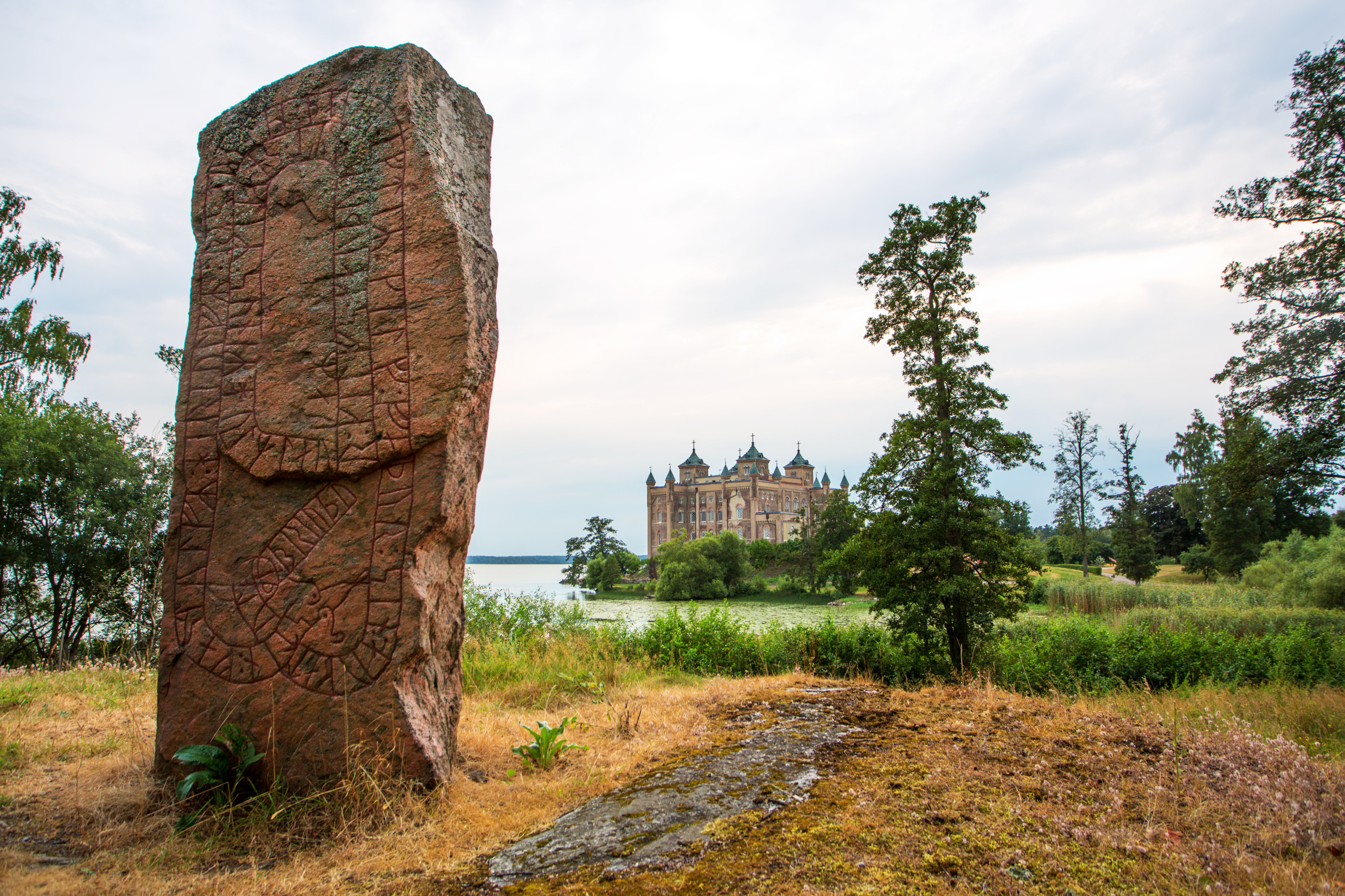 Une pierre avec des gravures runiques au premier plan, et le château de Stora Sundby en arrière-plan.