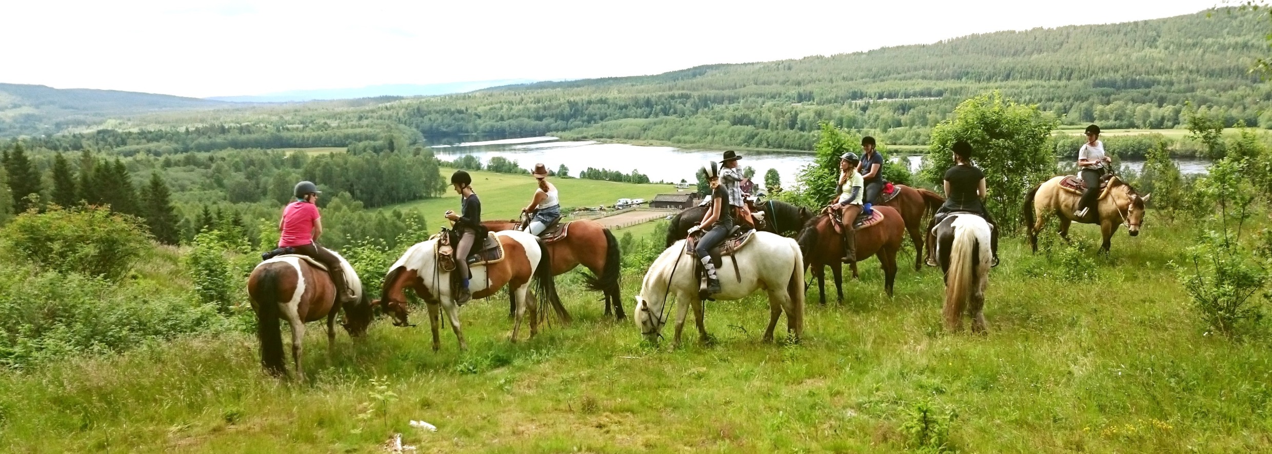 Een groep ruiters te paard pauzeert bij een uitkijkpunt bij Sundance Ranch, met een brede beboste vallei en rivier op de achtergrond.