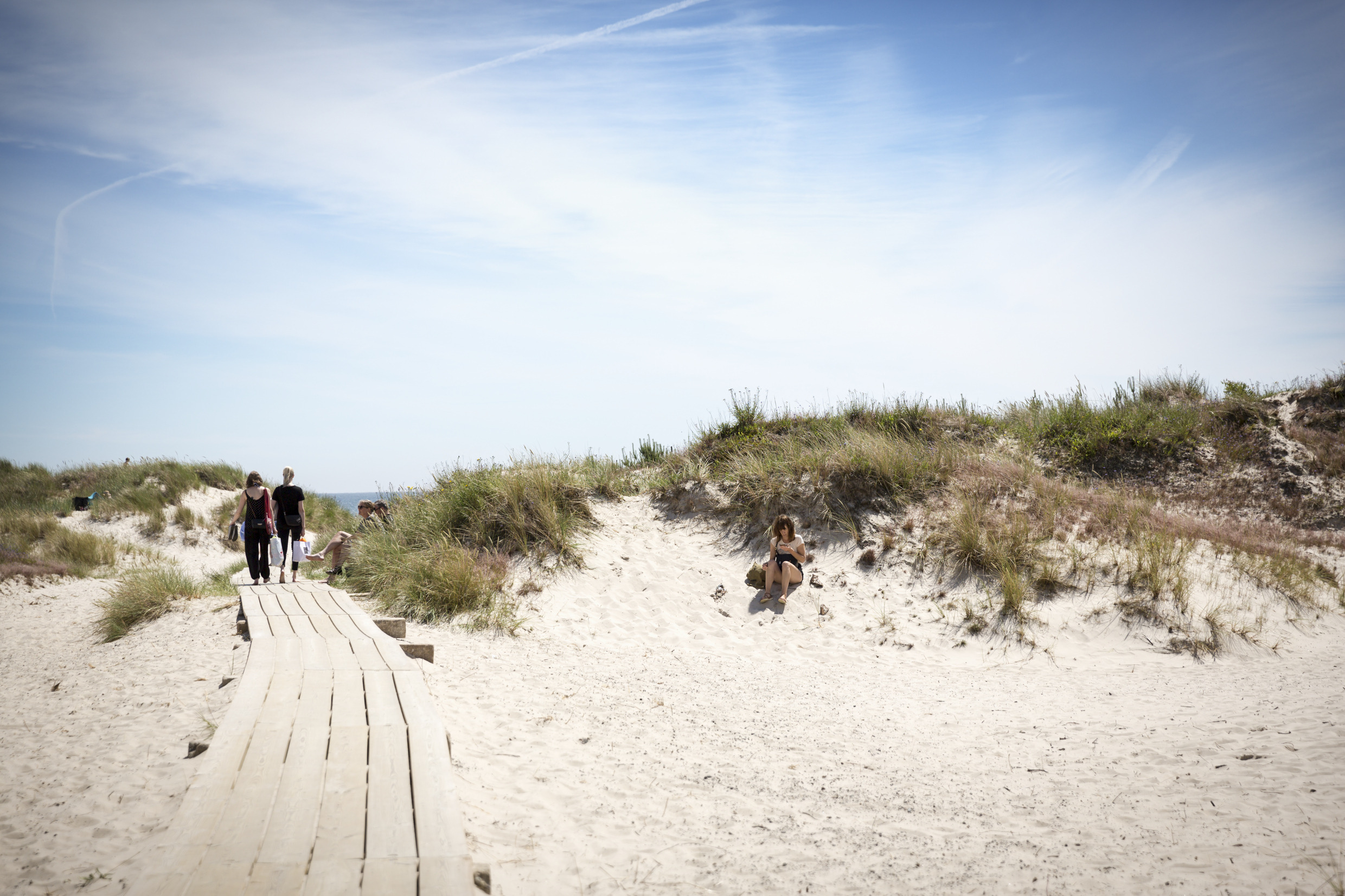 Une passerelle en bois traverse des dunes de sable blanc parsemées d'herbe.