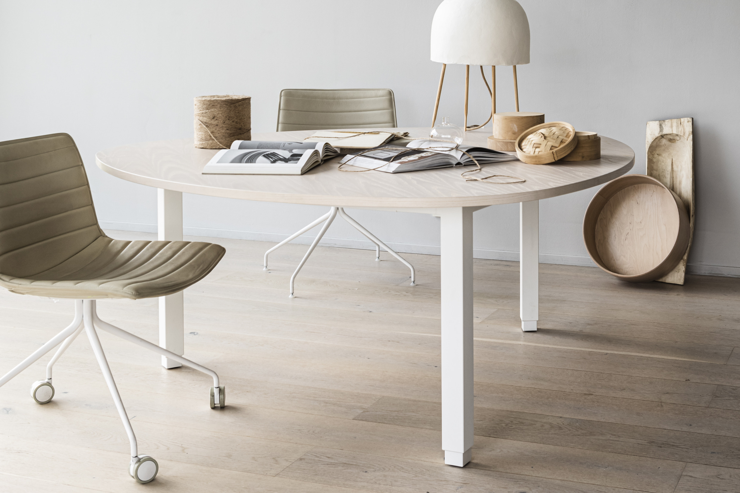 Ein Designertisch aus hellem Holz auf einem hellen Holzboden. Daneben steht ein Bürostuhl auf Rollen. Auf dem Tisch liegen zwei aufgeschlagene Bücher und zwei Holzgefäße.