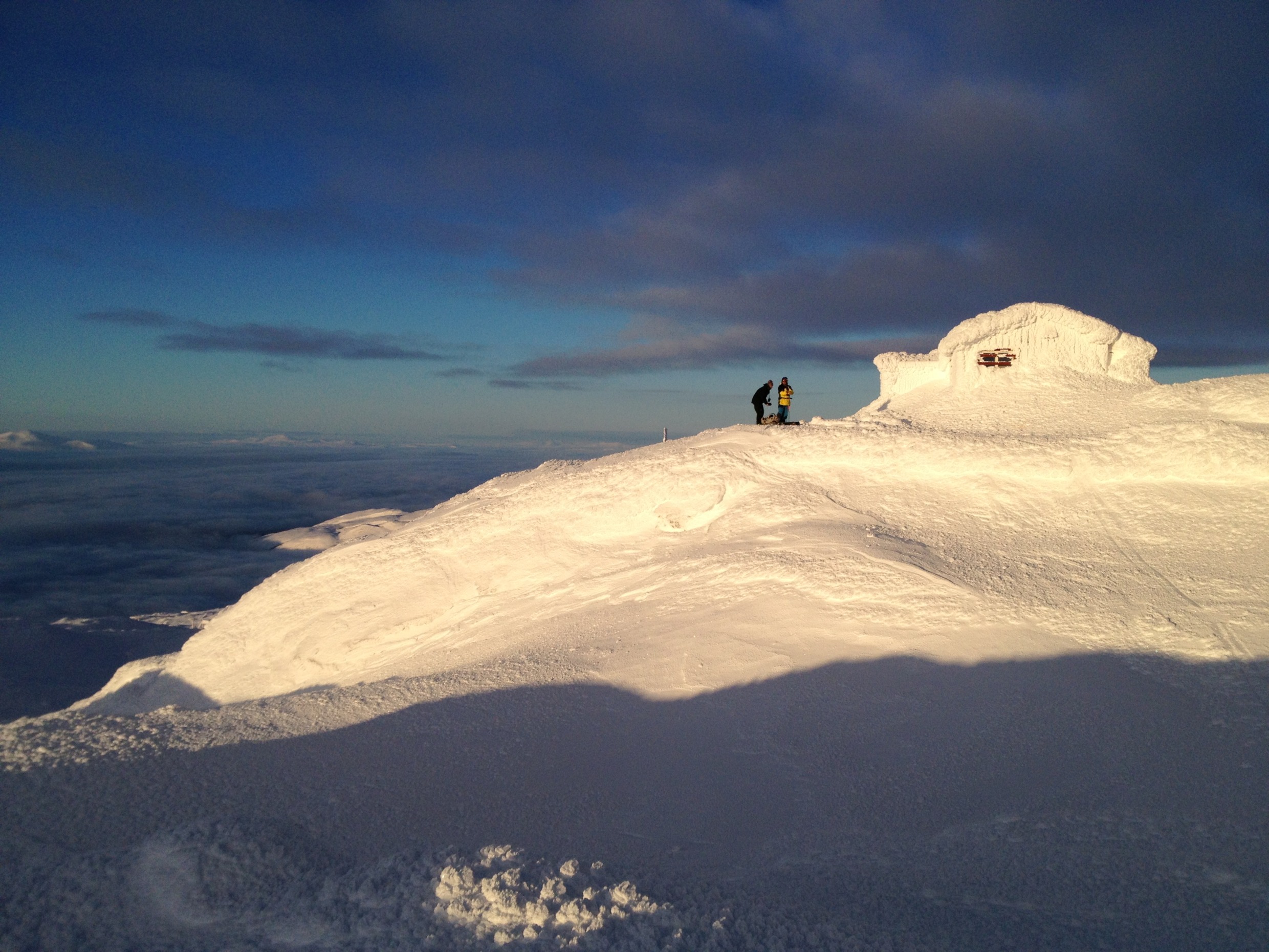 Zwei Leute vor dem Toppstugan in Åre, dem höchstgelegenen Café Schwedens, umgeben von schneebedeckten Hängen unter einem klaren Winterhimmel.