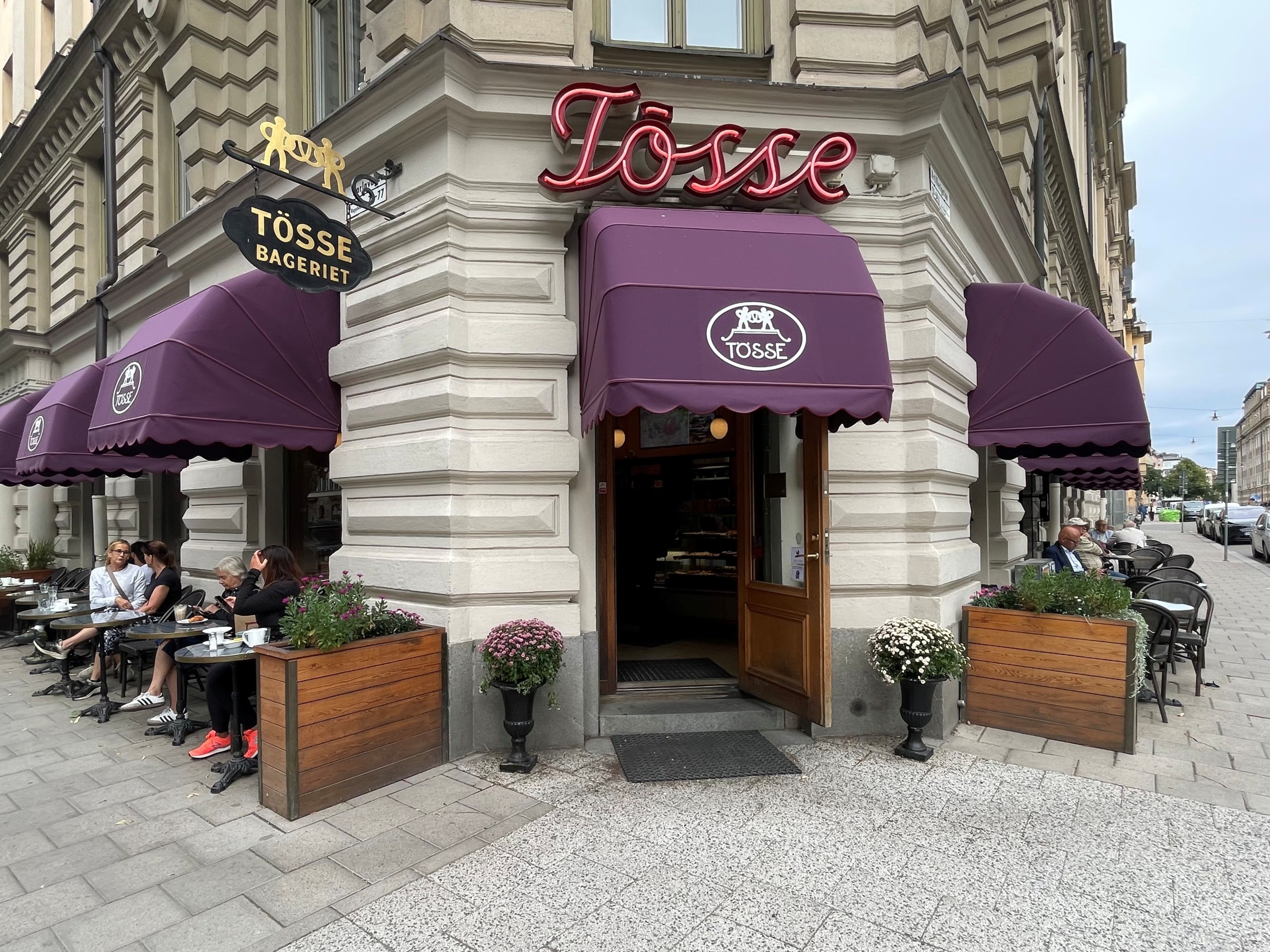 A white building with purple awnings and a sign that says ‘Tösse’ at the entrance door.