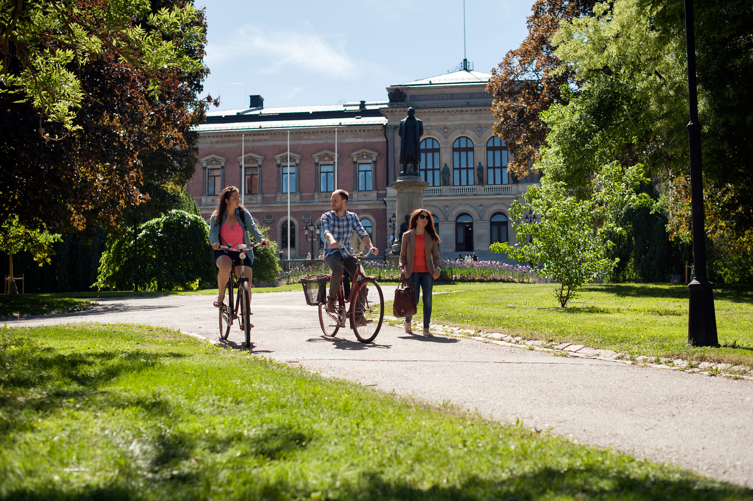 A man and a woman bike past a pedestrian woman at the Uppsala Univerity campus.