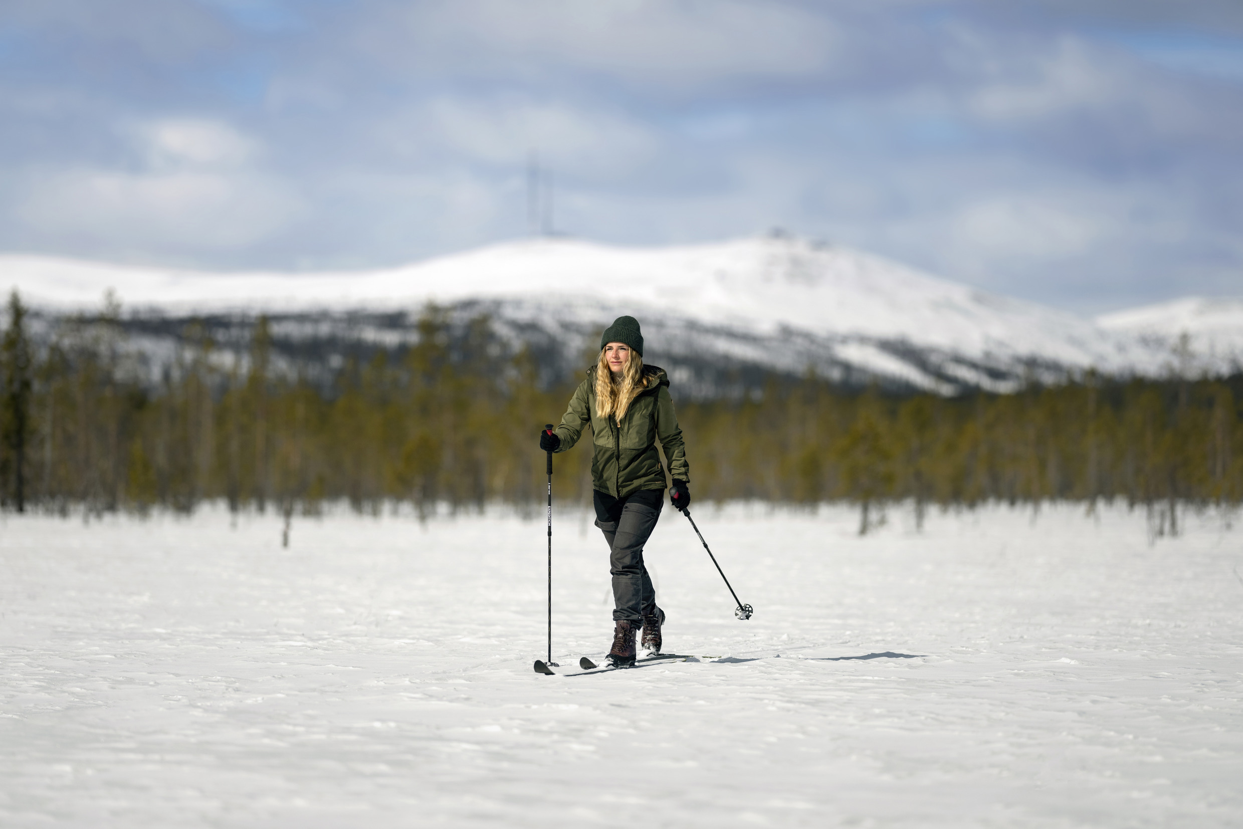 Une personne pratiquant le ski de fond sur un terrain enneigé, avec une forêt et des montagnes en arrière-plan, près de Gällivare.