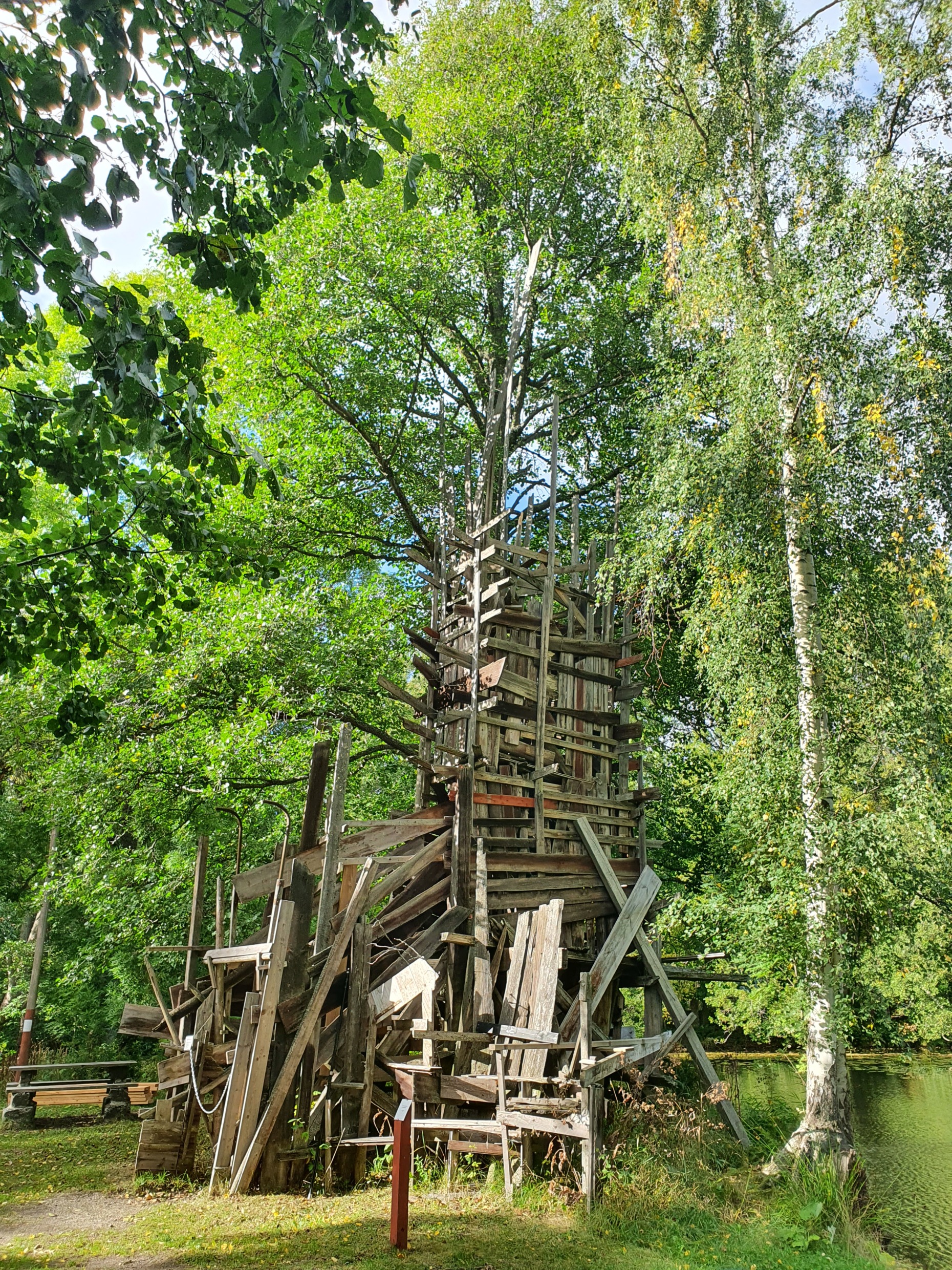 A sculpture called “Service Tower Life Lie” made of wooden planks in a lush green environment in a sculpture park.