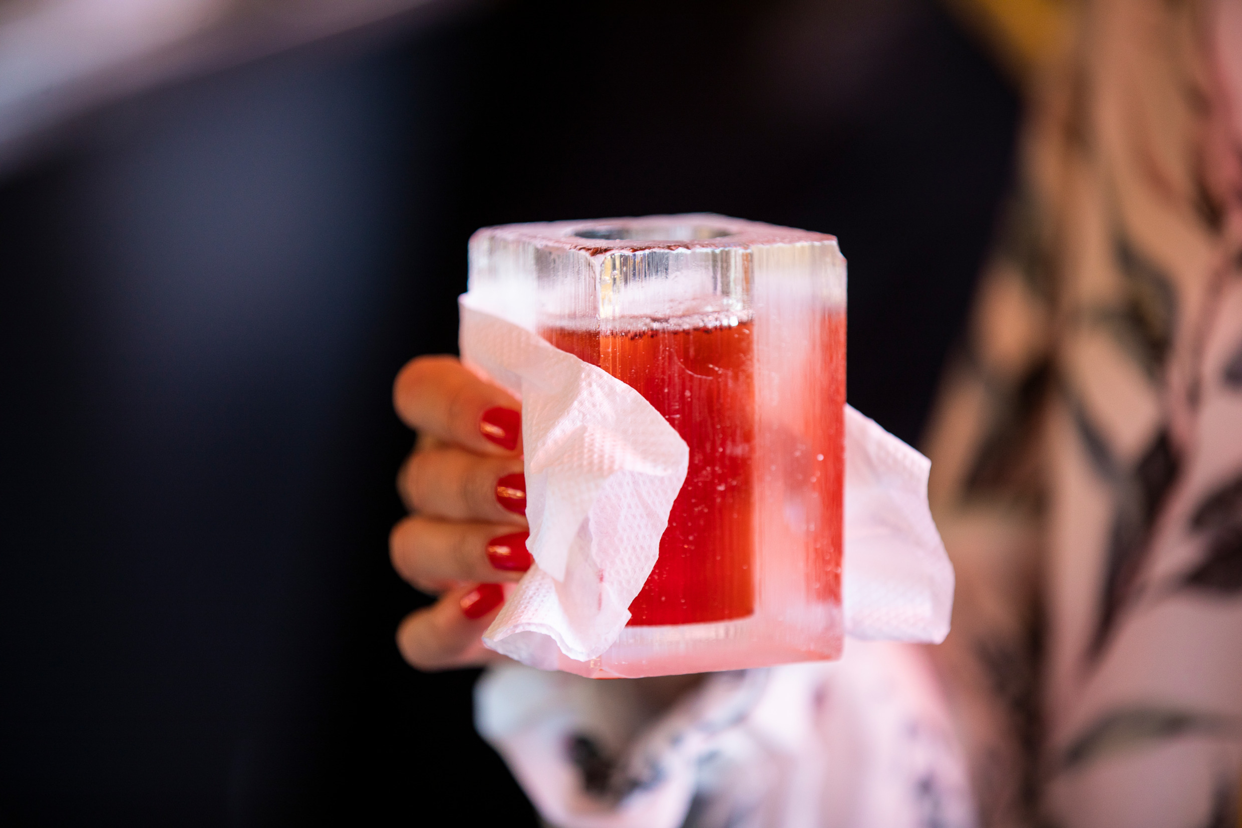Someone holding a glass of ice with a napkin, with red beverage inside.