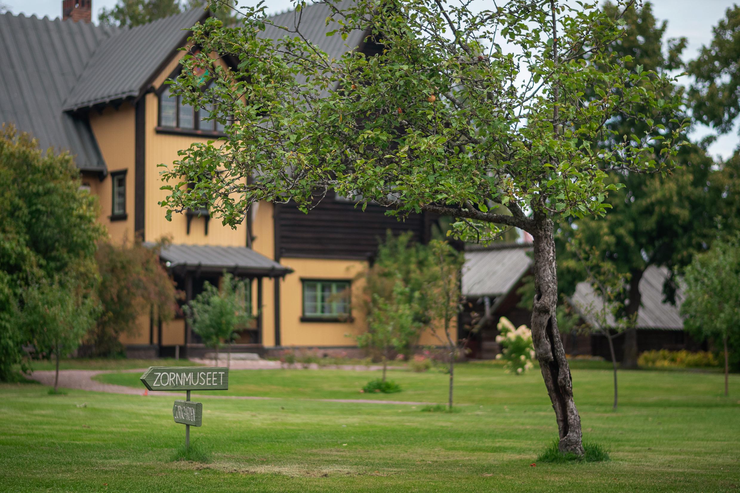 In the foreground are lush trees and a small wooden sign reading 'Zorn Museum', with the museum building in the background.