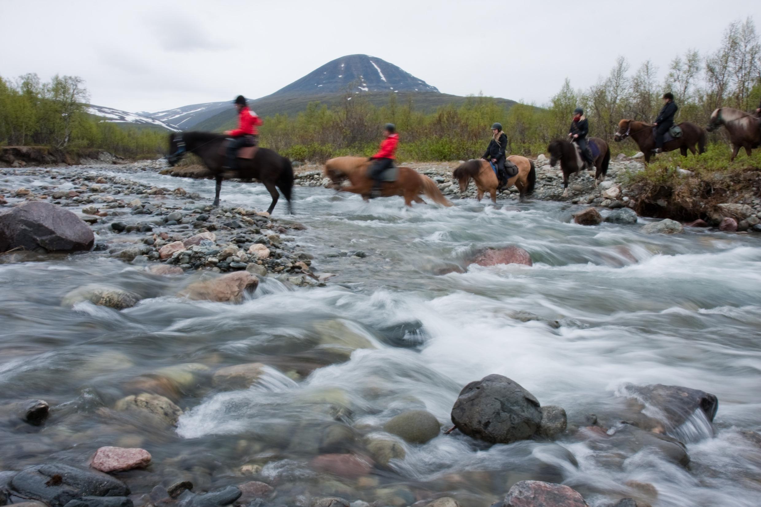 Mensen te paard steken een beek over in Zweeds Lapland.