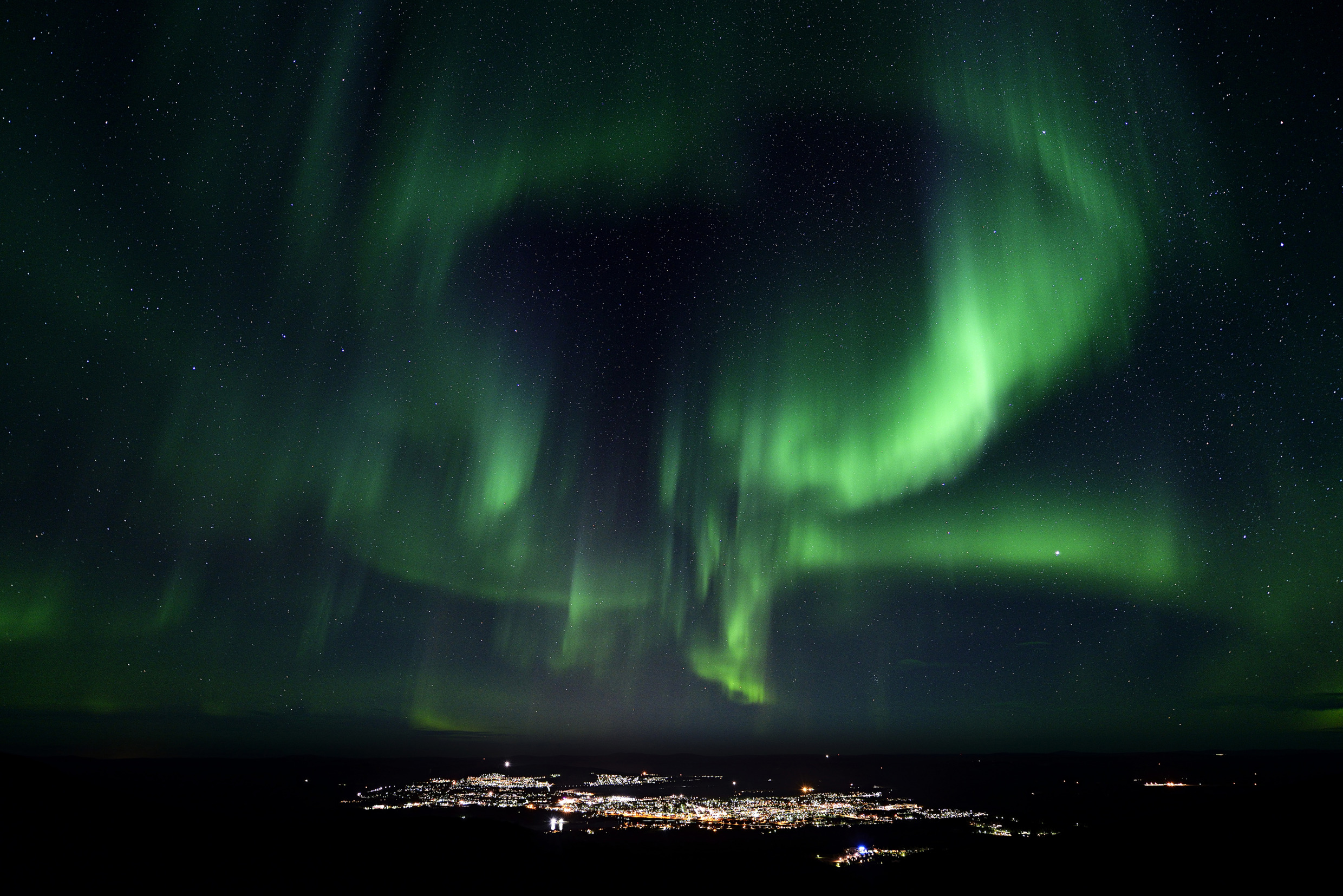 Green aurora lighting up the night sky above Gällivare and its city lights.