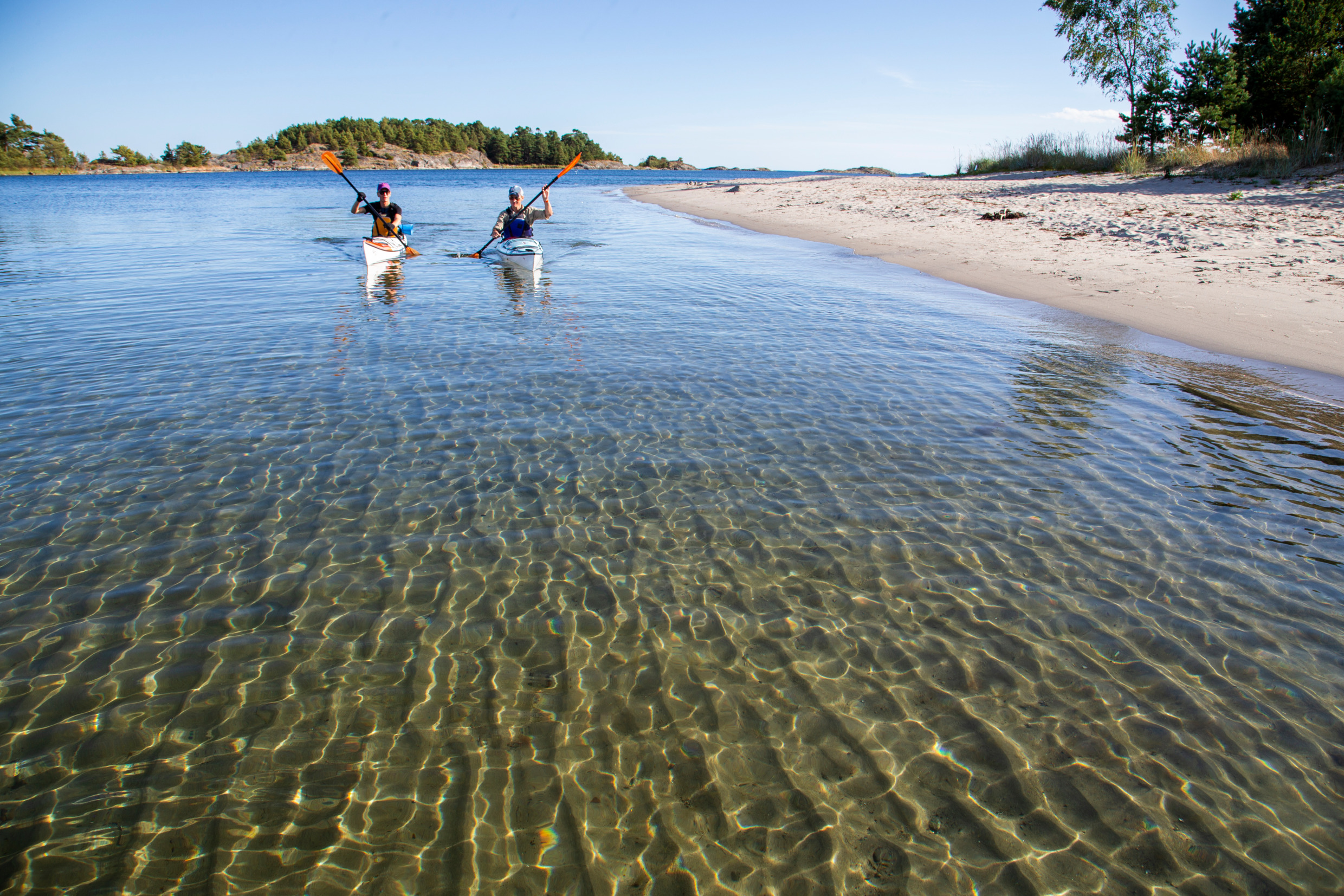 Two people are kayaking in shallow water near an island.