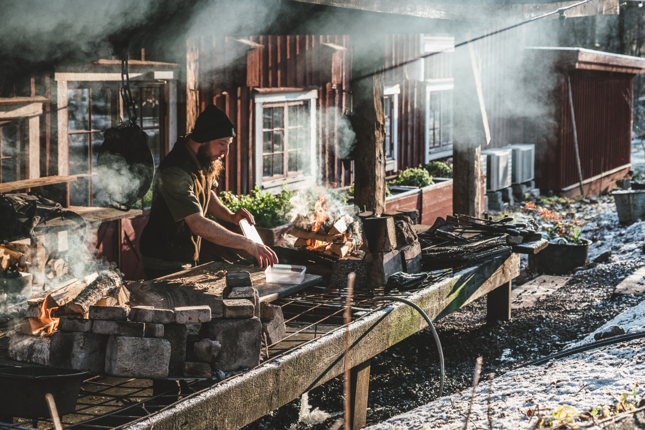 Chef cooking over open fire at outdoor station in winter outside Knystaforsen restaurant in Halland.