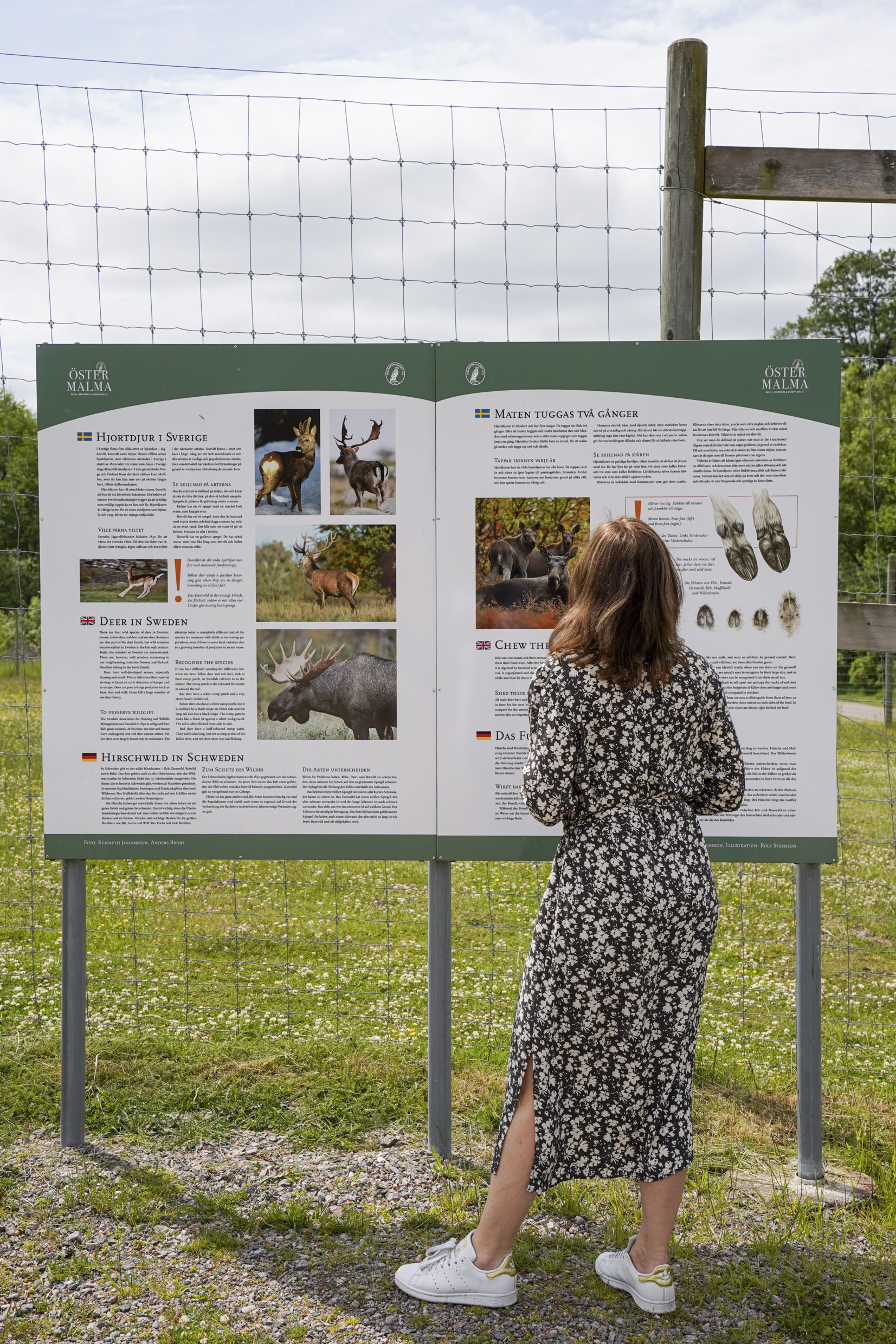 Een vrouw bekijkt een informatiebord over de verschillende dieren in het park.