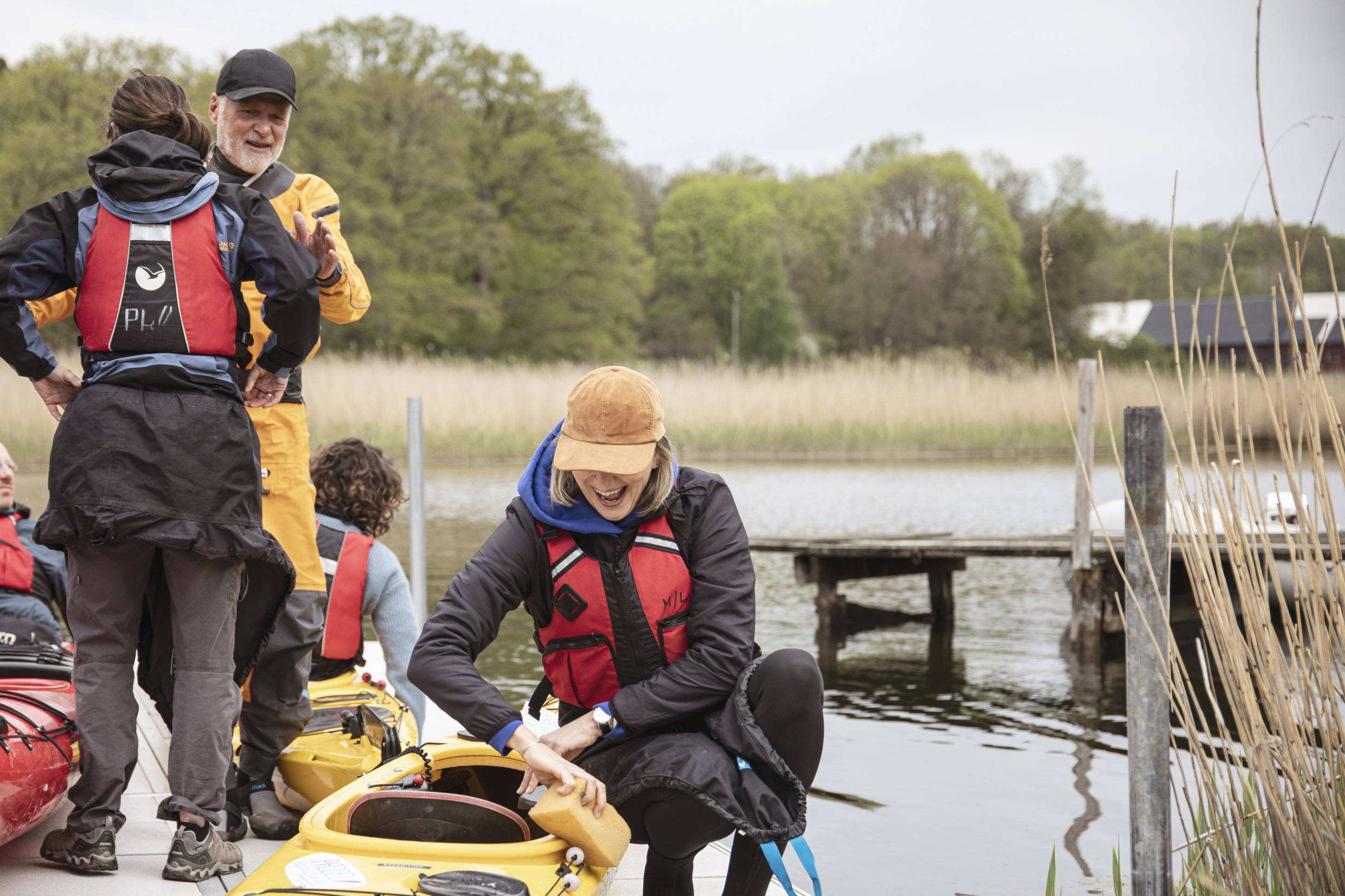 A group of people are on a jetty preparing their kayaks. The guide is dressed in orange and he is smiling.