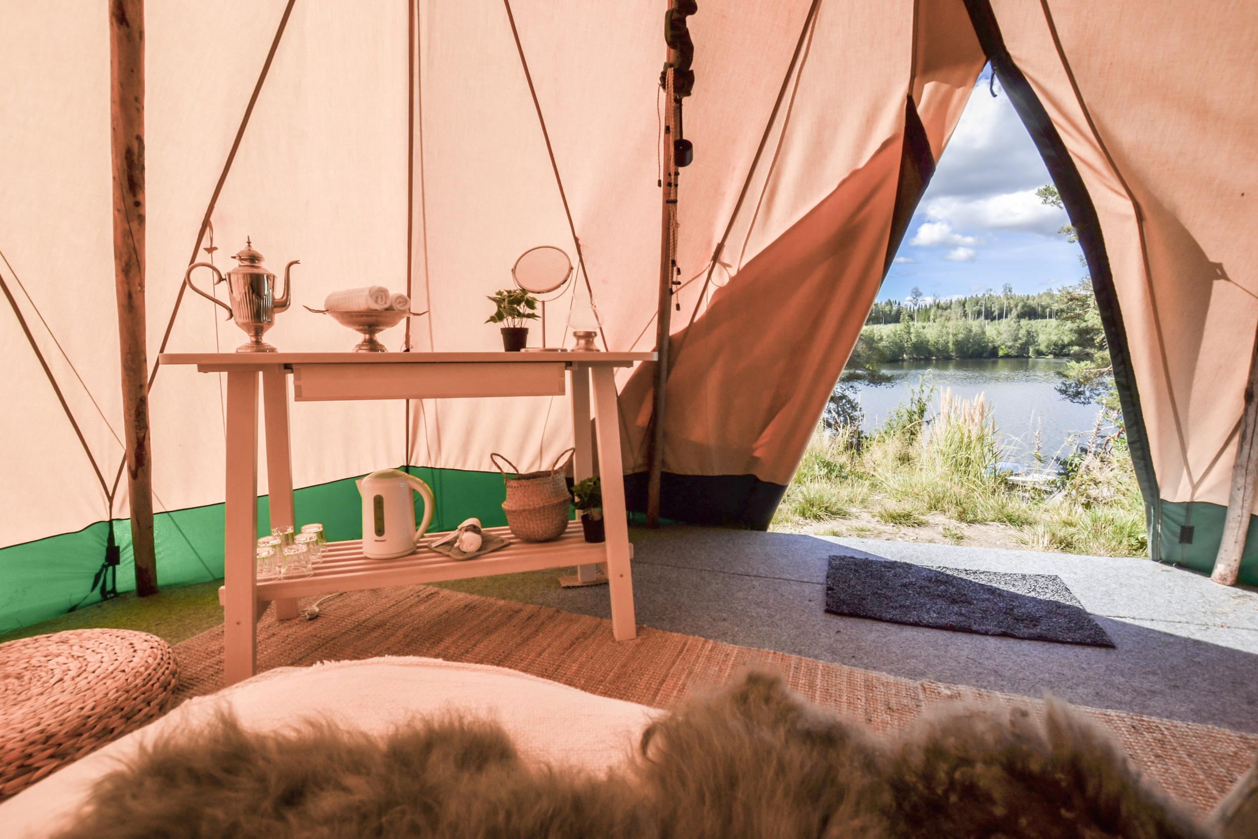 Blick aus dem Inneren eines Tipi-Zeltes. Draußen sind ein Wald und ein See zu sehen.