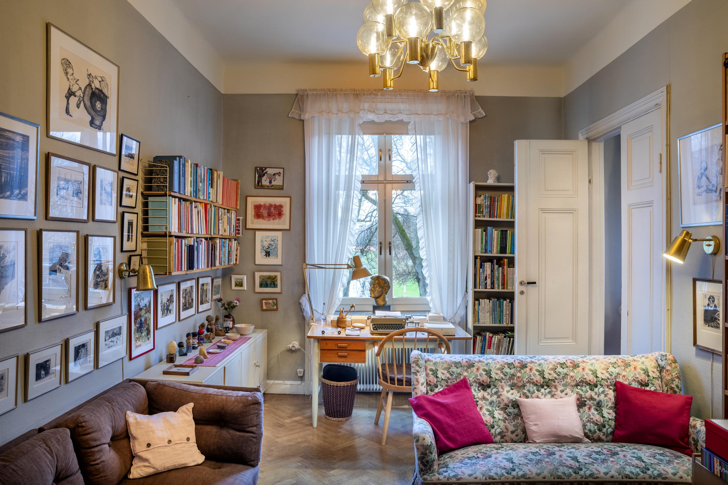 Das Innere eines Zimmers, das dicht mit einem Schreibtisch, Sofas, Bücherregalen und Kunst an den Wänden gefüllt ist.