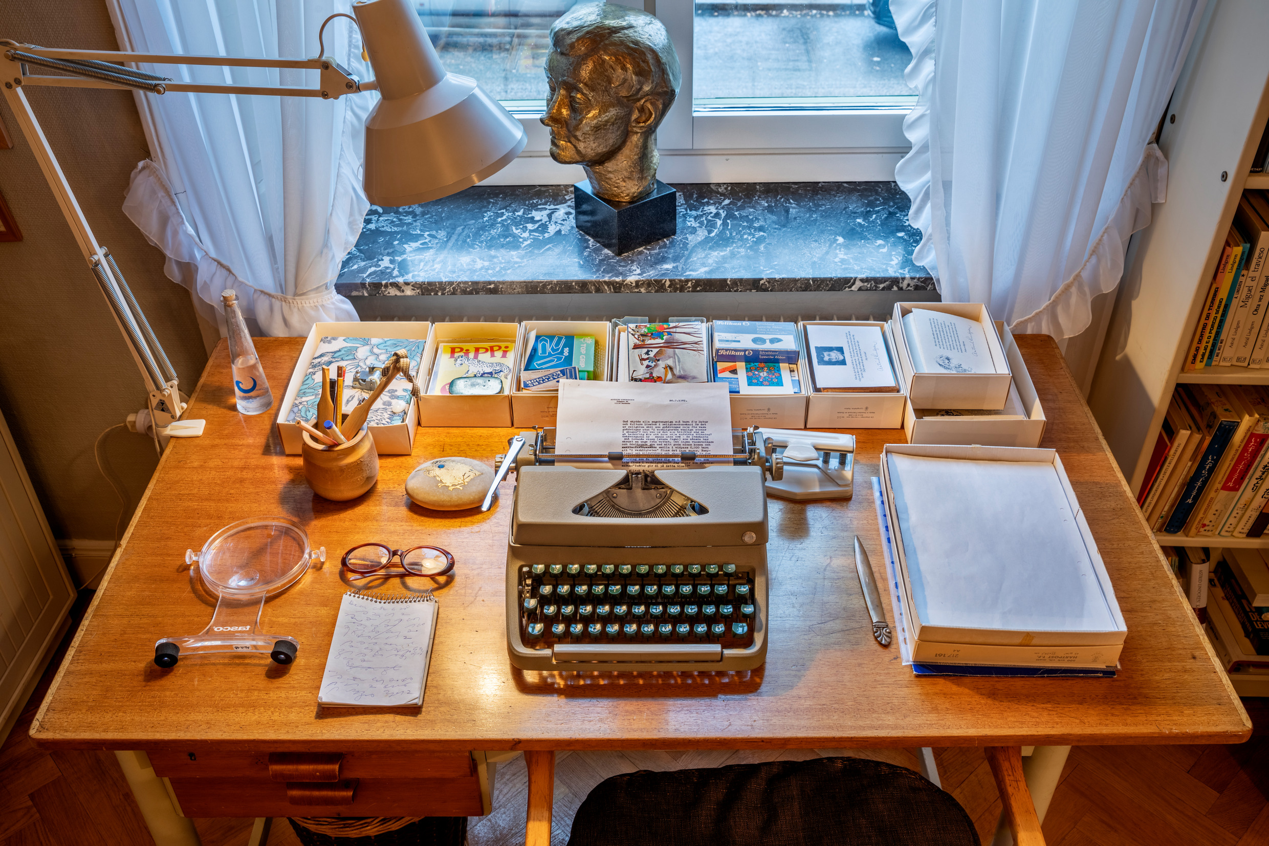 A desk with a reading lamp, a typewriter, books and other artifacts.