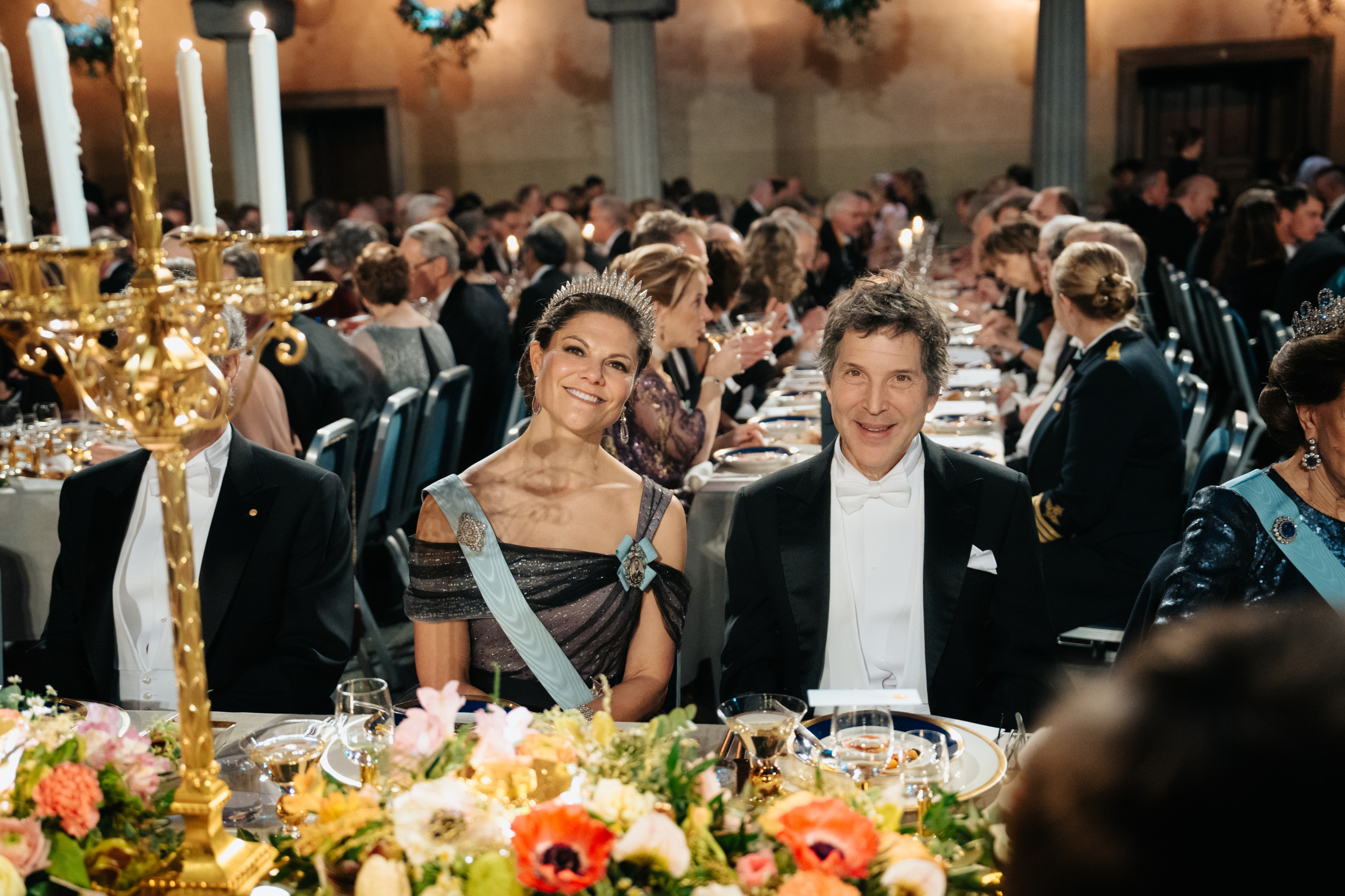 Crown Princess Victoria and David Baker seated at the Nobel Prize banquet table, surrounded by flowers and guests.