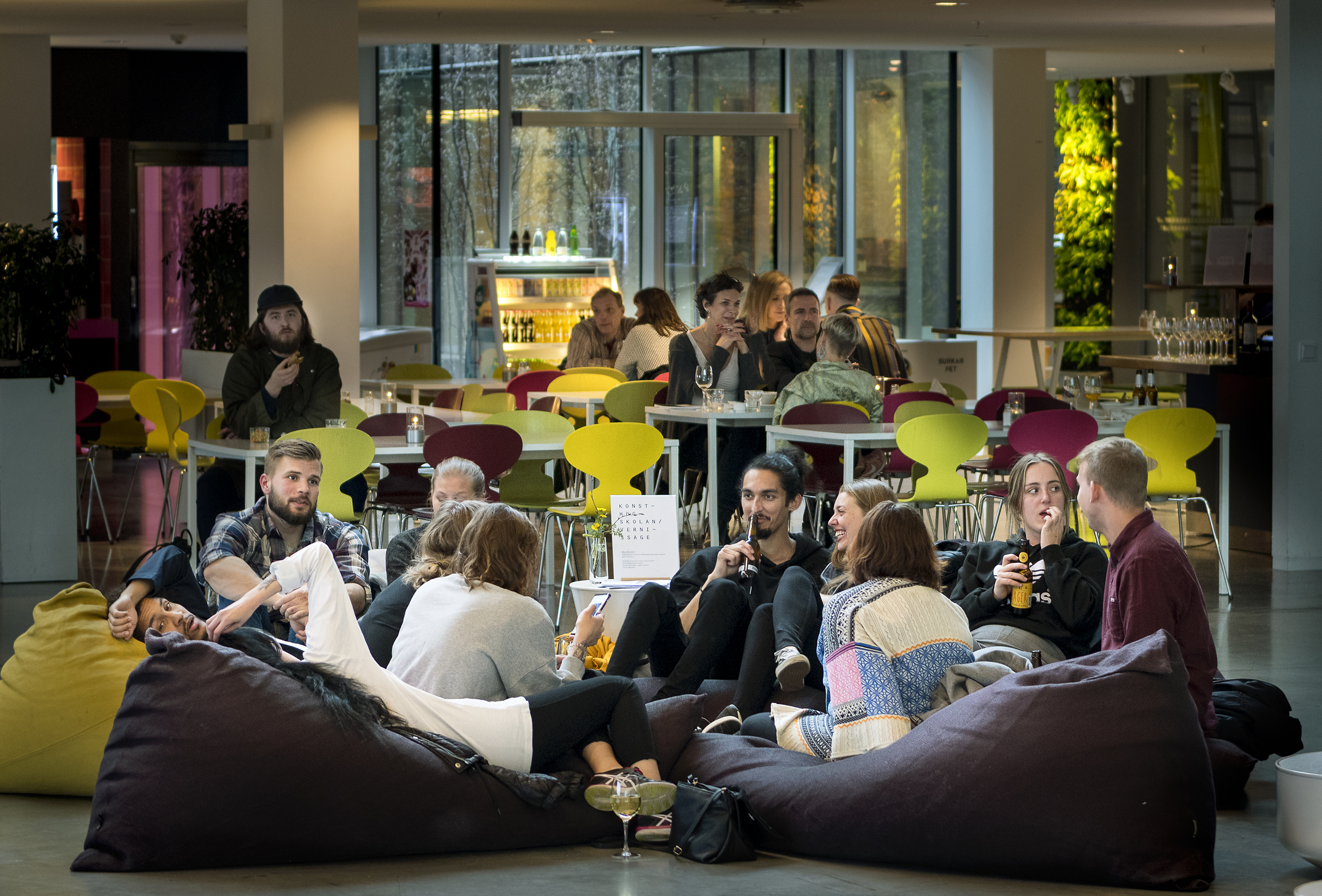 Visitors chat and relax on beanbags at an Art Friday event at Bildmuseet in Umeå, with colourful chairs and café tables in the background.