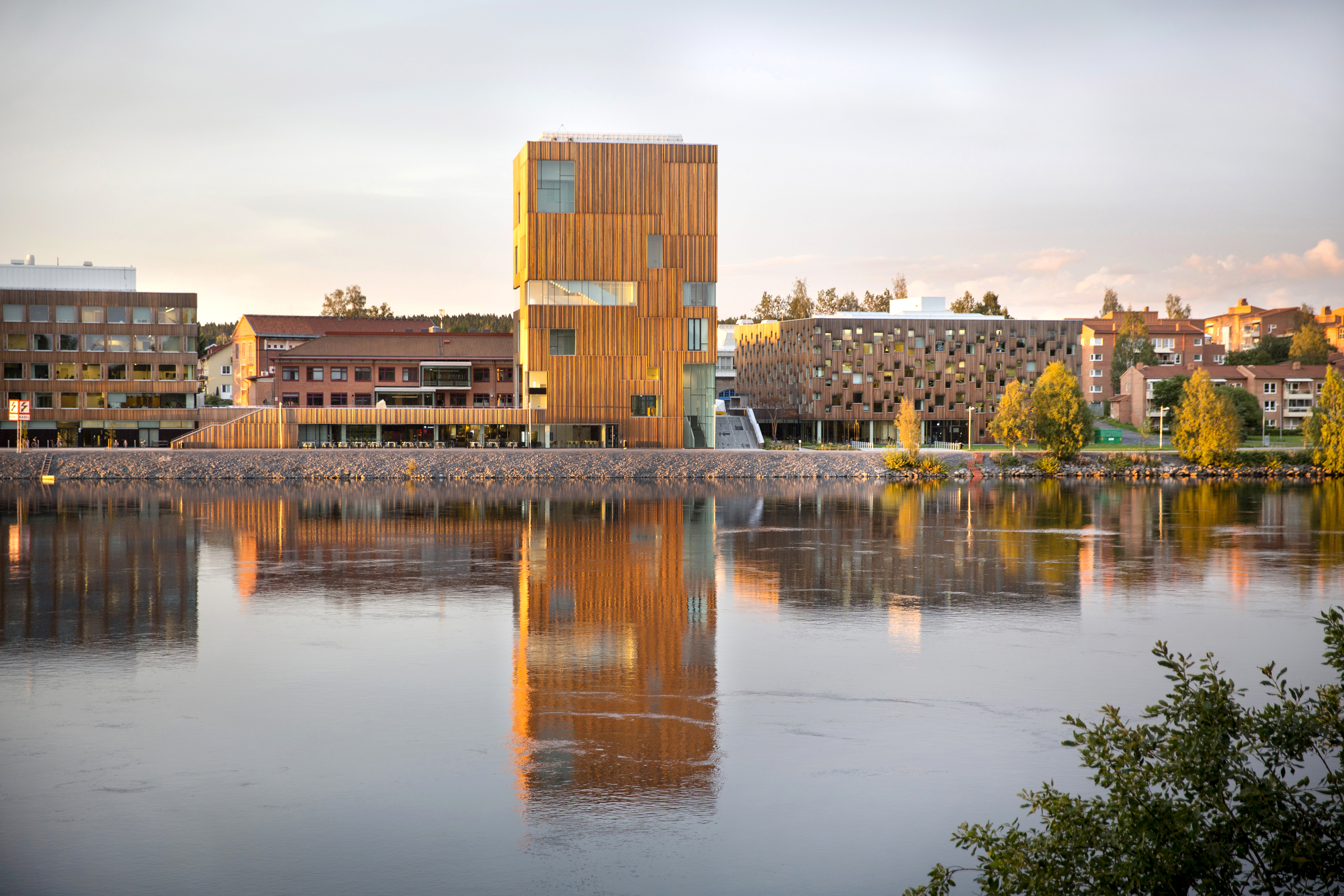 Bildmuseet’s tall, wood-clad building beside the Ume River in Umeå, reflected in the calm water in the warm evening light.
