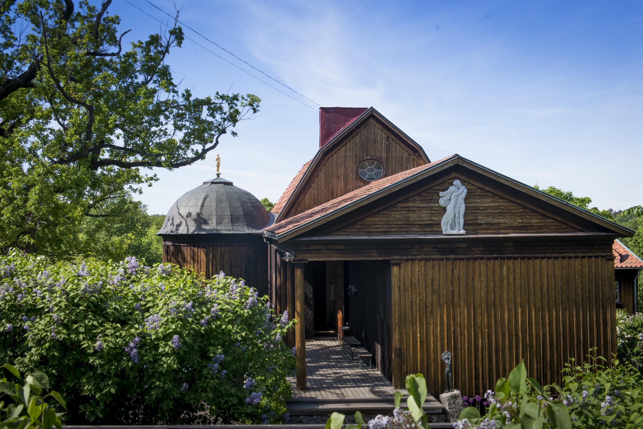 The wooden house of Carl Eldh is surrounded by greenery, and designed in different levels and shapes with sculptures on and by the building.