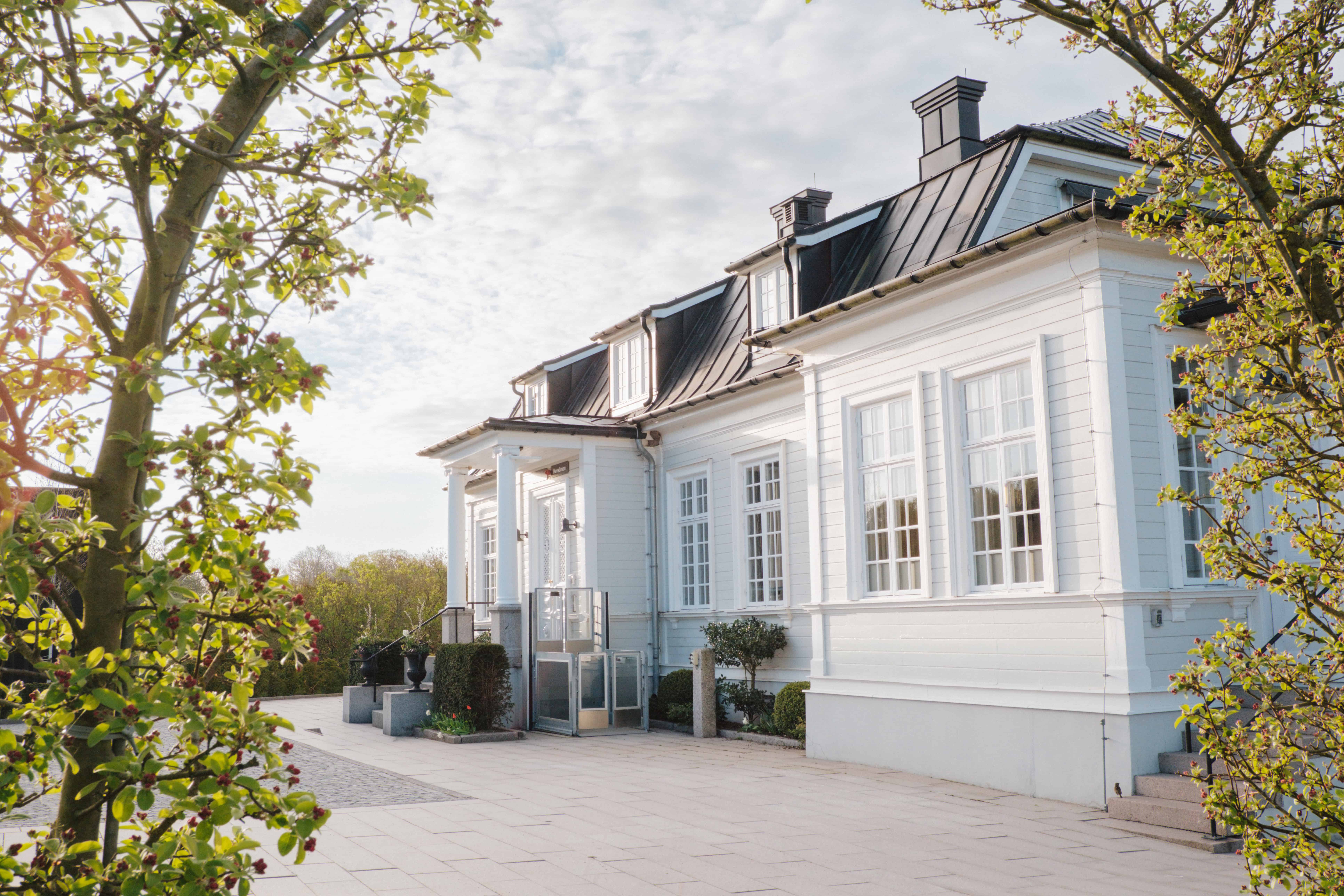 White manor house surrounded by leafy trees and greenery.