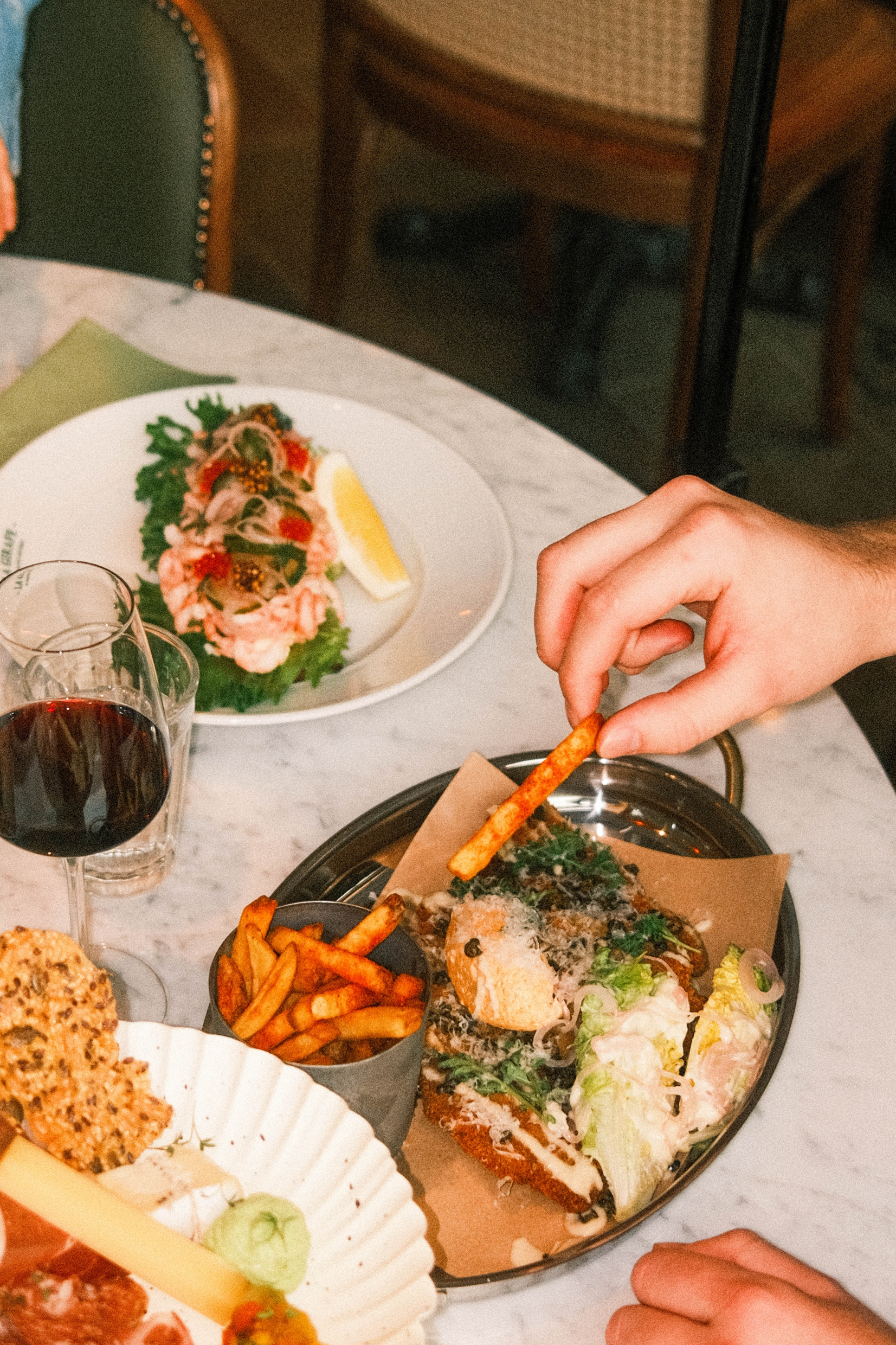 Close-up of several small dishes on a marble table at La Girafe, including fries, toast, prawns, cheese and charcuterie.