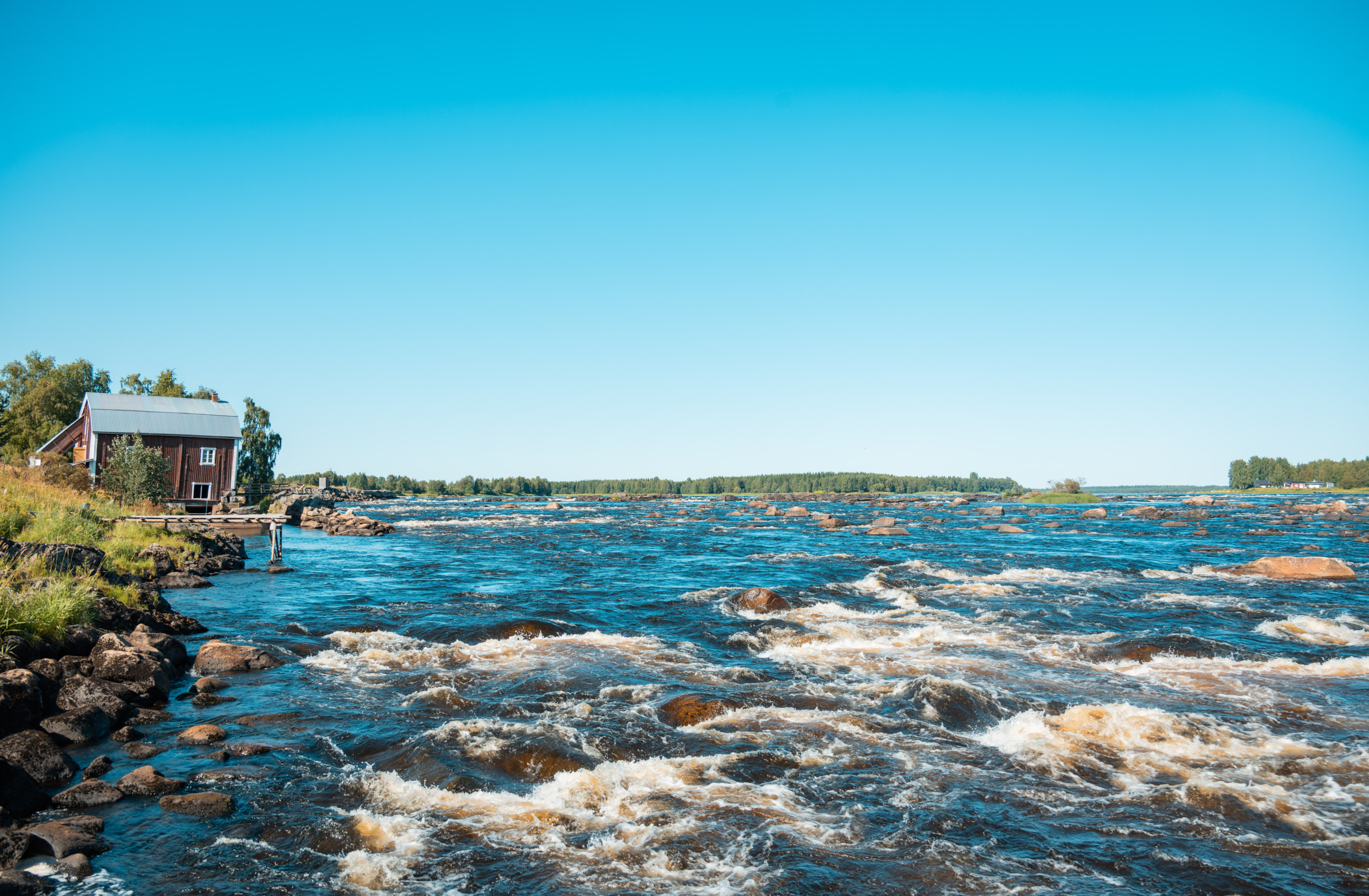 A picture of the Torne River with a wooden house at the water's edge to the left.