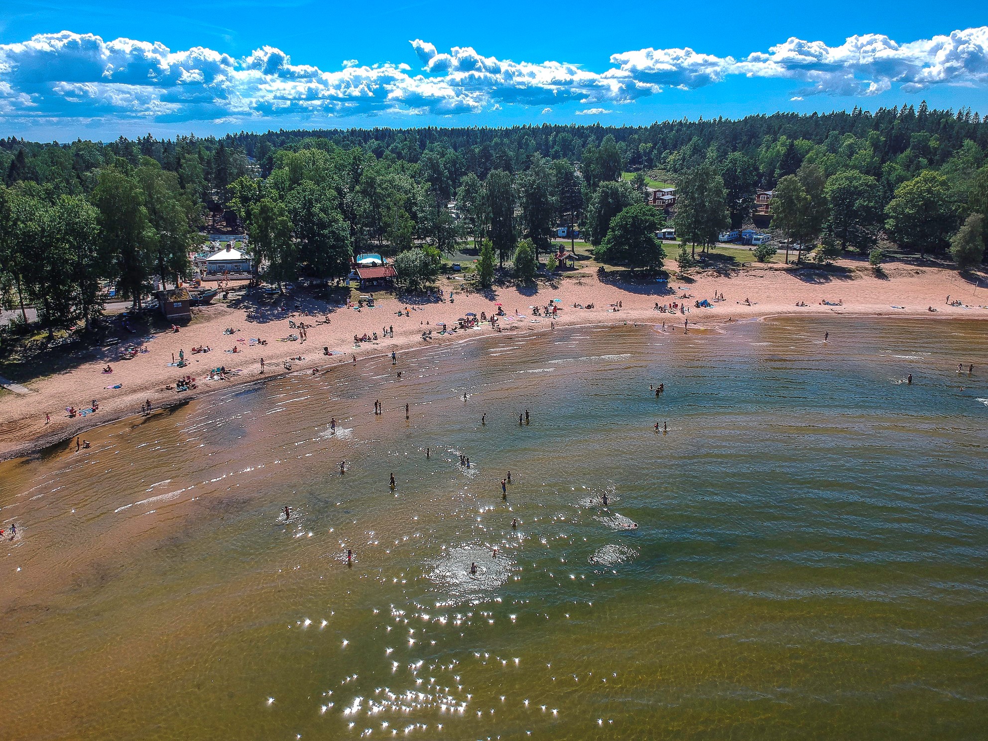 Aerial view of a sandy beach by Lake Vänern with people swimming and relaxing.