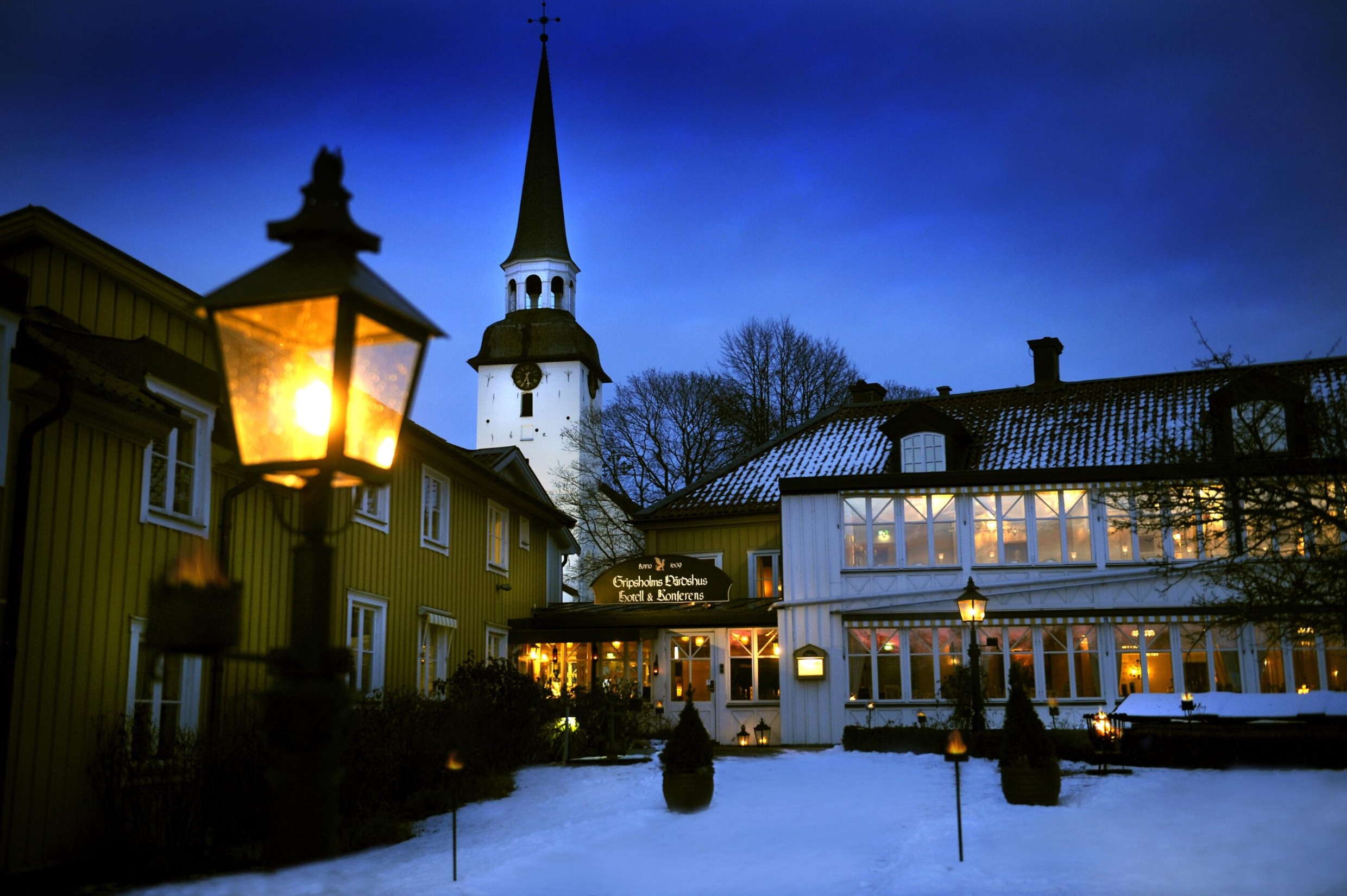 Gripsholm Inn with glowing lanterns, wooden façades and a church tower in the background, Mariefred.