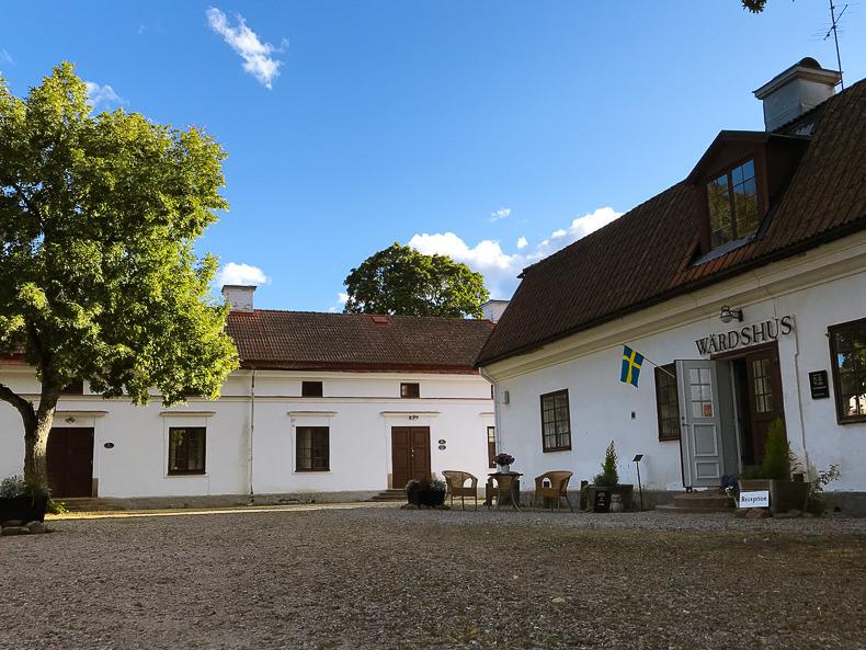 Twee huizen met witte gevels. Een paar tuinmeubelen staan langs een van de huizen op het erf.