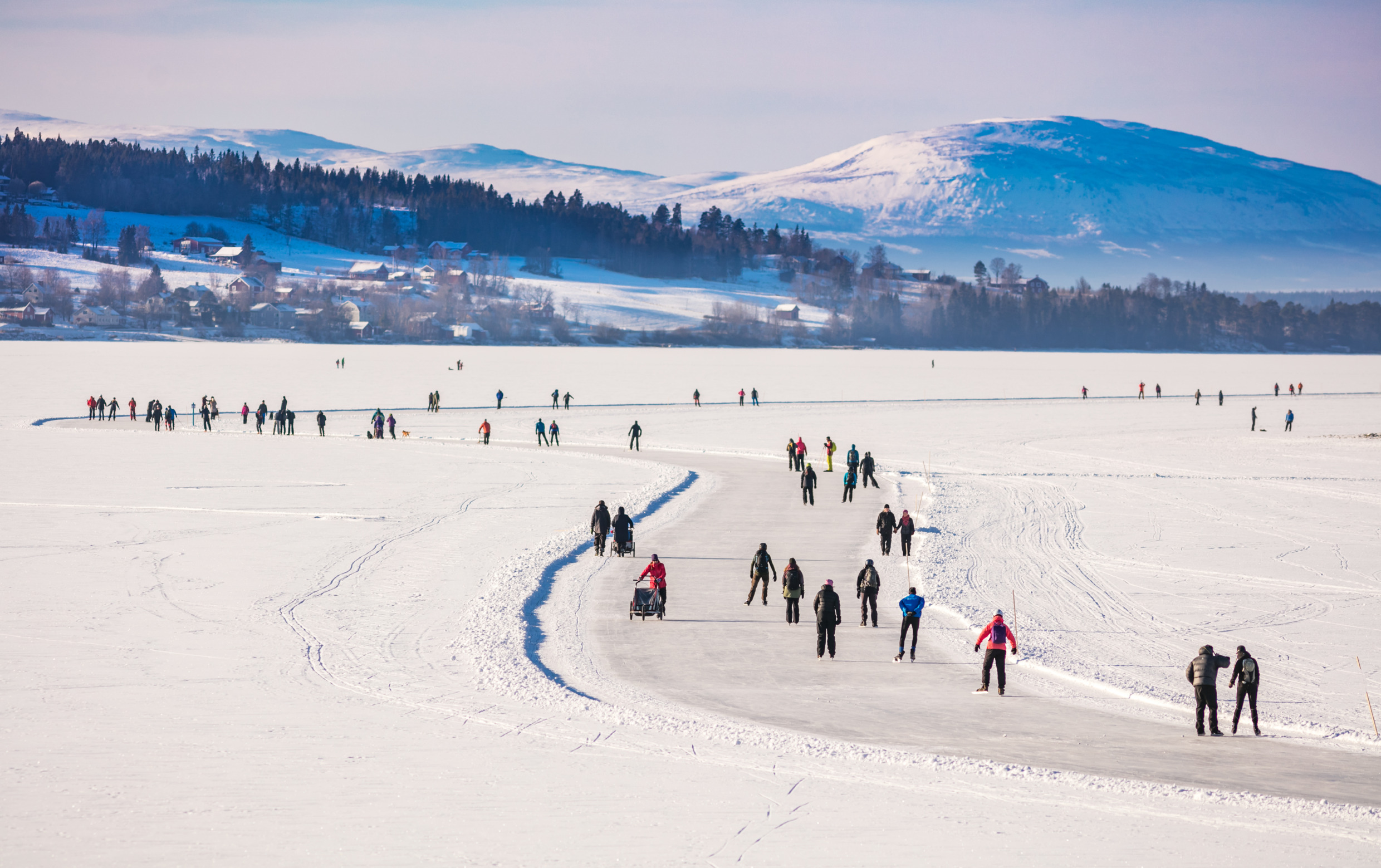 People ice skating on the pre-made tracks on Lake Storsjön on a sunny winter day in Östersund.