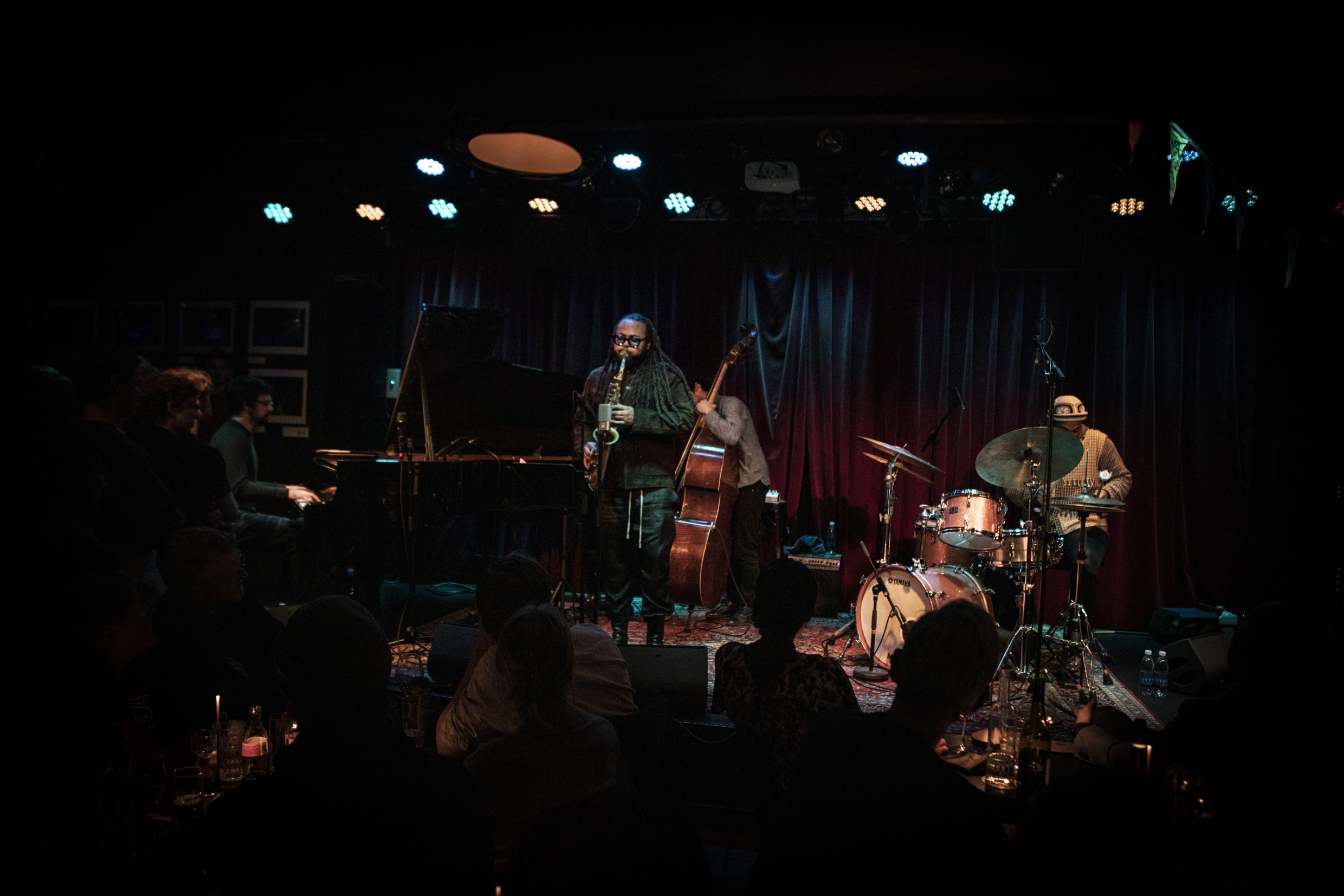 Jazz band performing on stage in a dimly lit venue during Stockholm Jazz Festival, with saxophonist, pianist, drummer and double bassist.