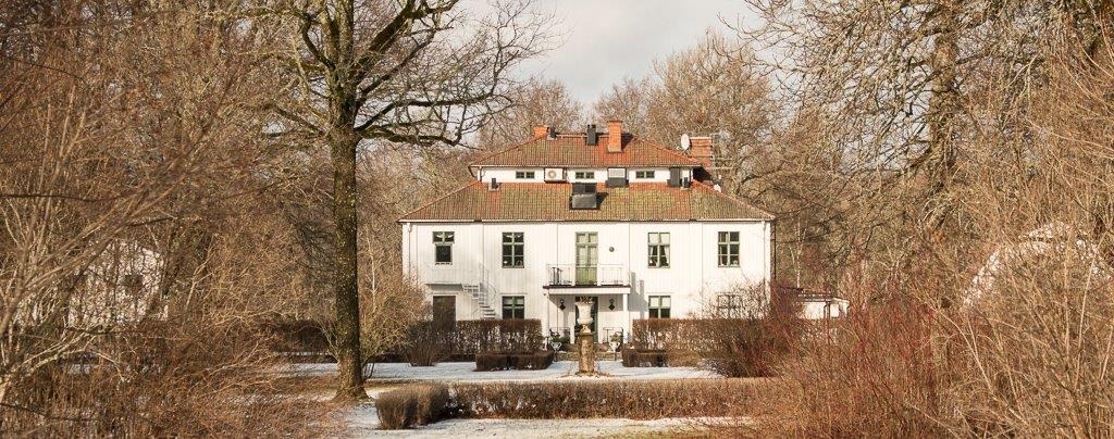 White wooden castle framed by leafless trees in winter light, Noors Castle in Knivsta.