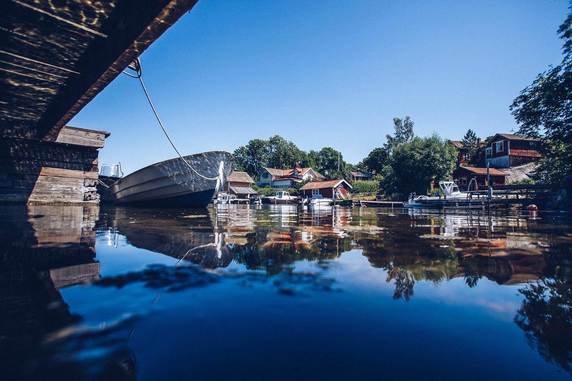 A old fishing port with several small boats seen from the sea. Cottages and greenery along the shore.