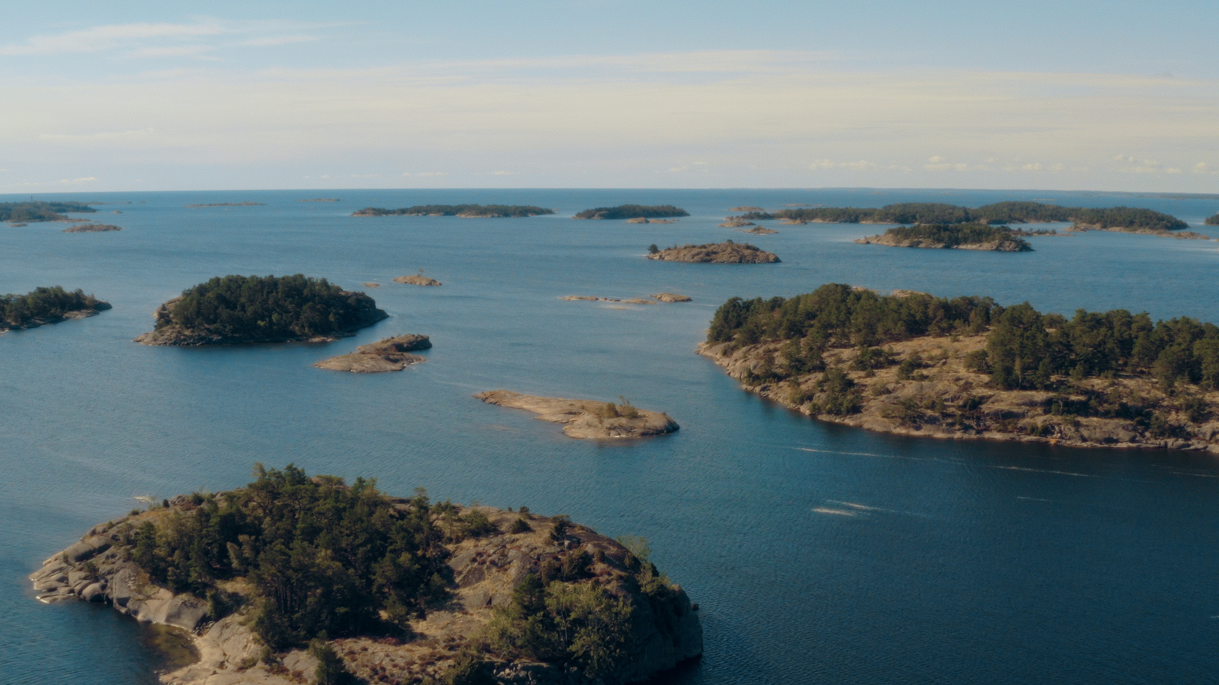 A cluster of small Swedish rocky islands spreads across a wide expanse of blue water.