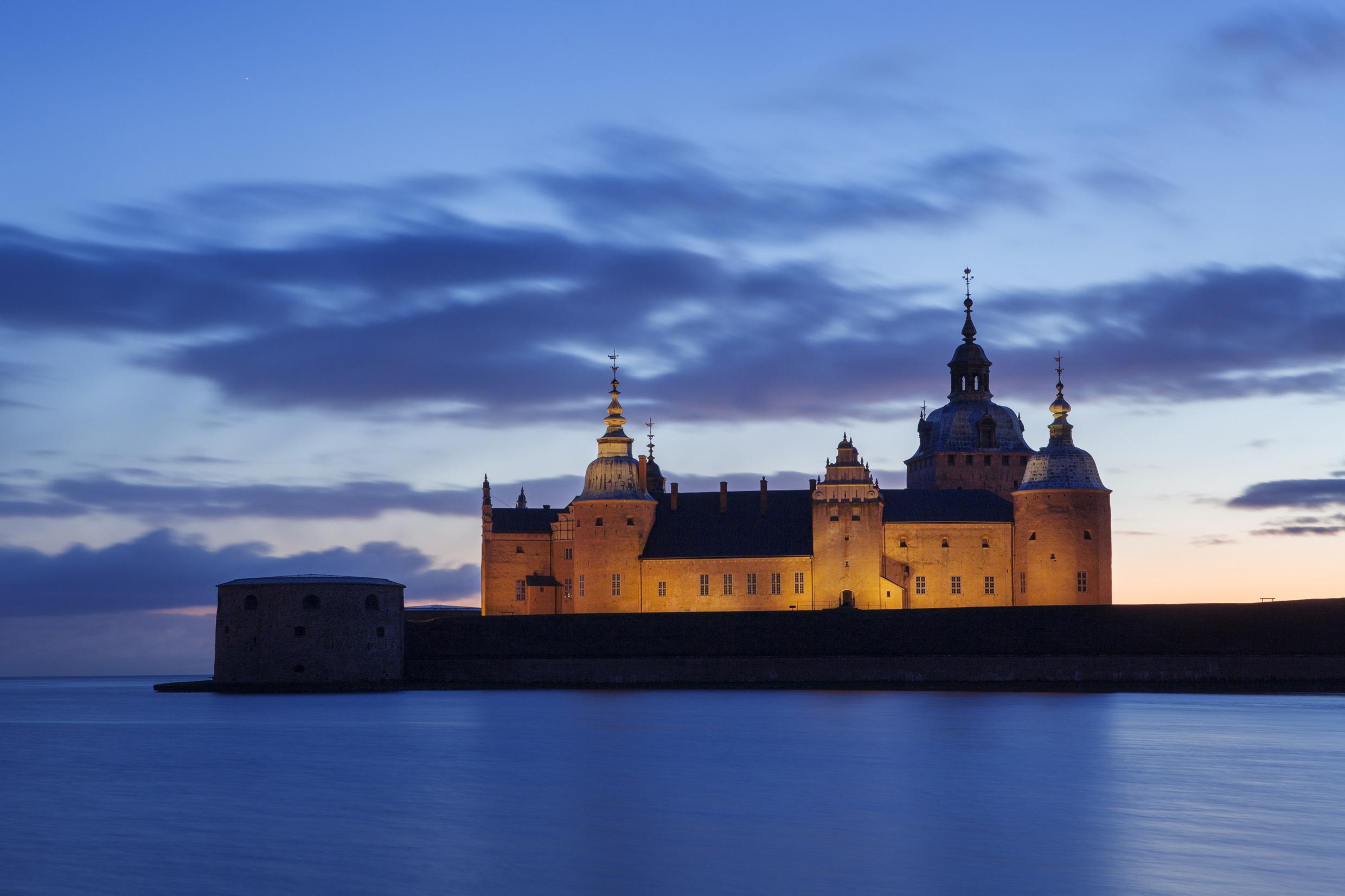 Die Vorderseite der Burg Kalmar wird von Scheinwerfern beleuchtet und ist von einem dämmrigen Himmel und der dunklen Ostsee umgeben.