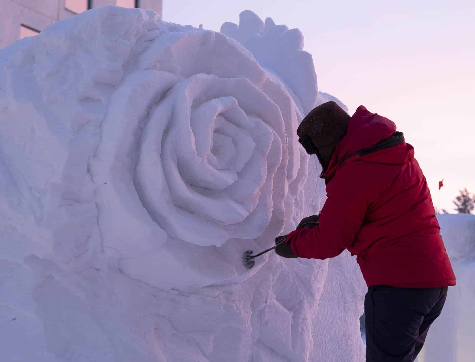 Une personne en train de sculpter une grande sculpture de neige lors du Festival de la neige de Kiruna, en hiver.