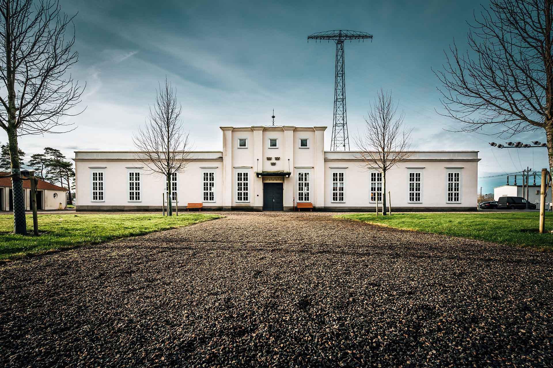 Een kind speelt in een park voor een wit stenen huis met een zendmast.