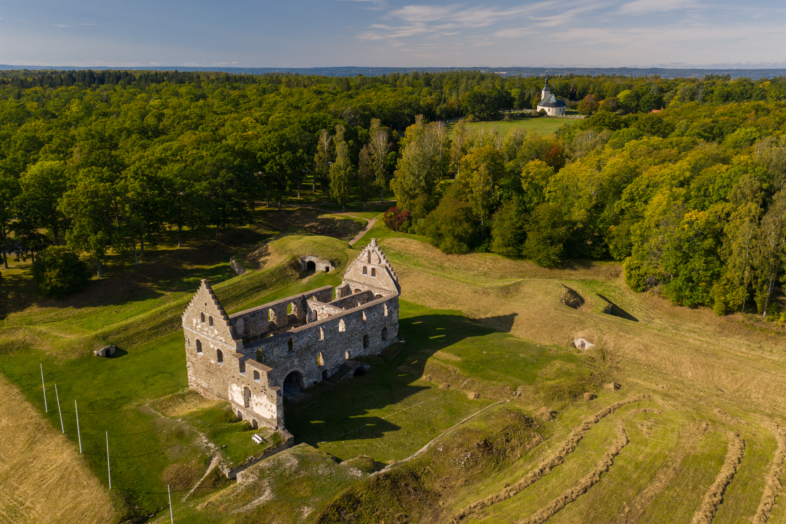 Luchtfoto van de ruïnes van Visingsborg Castle, omgeven door groene velden en bossen, met op de achtergrond de Brahekyrkan-kerk.
