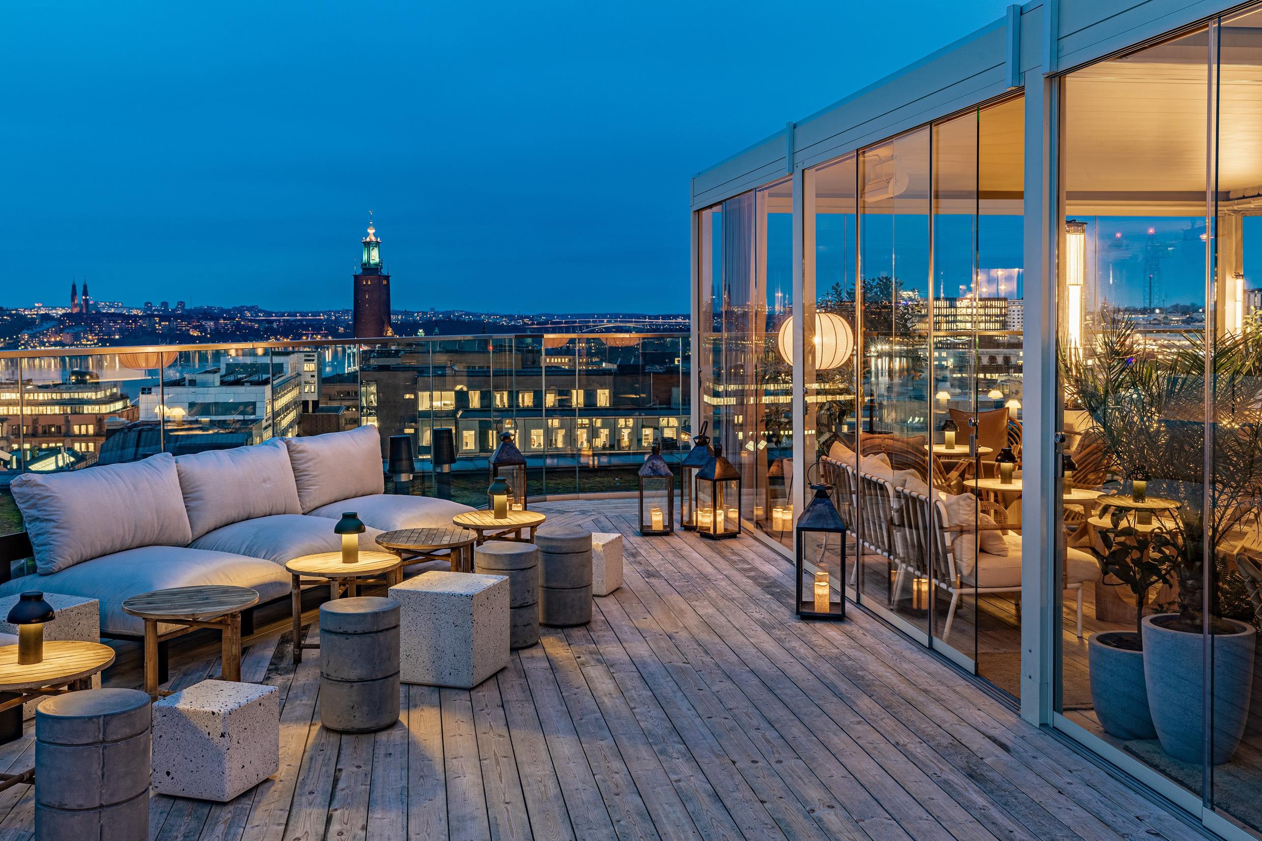 Eine stilvolle Außenbar auf einem Dach mit Blick auf Stockholm und das Rathaus. Auf der rechten Seite sehen Sie einen Teil, der hinter einer Glaswand liegt.
