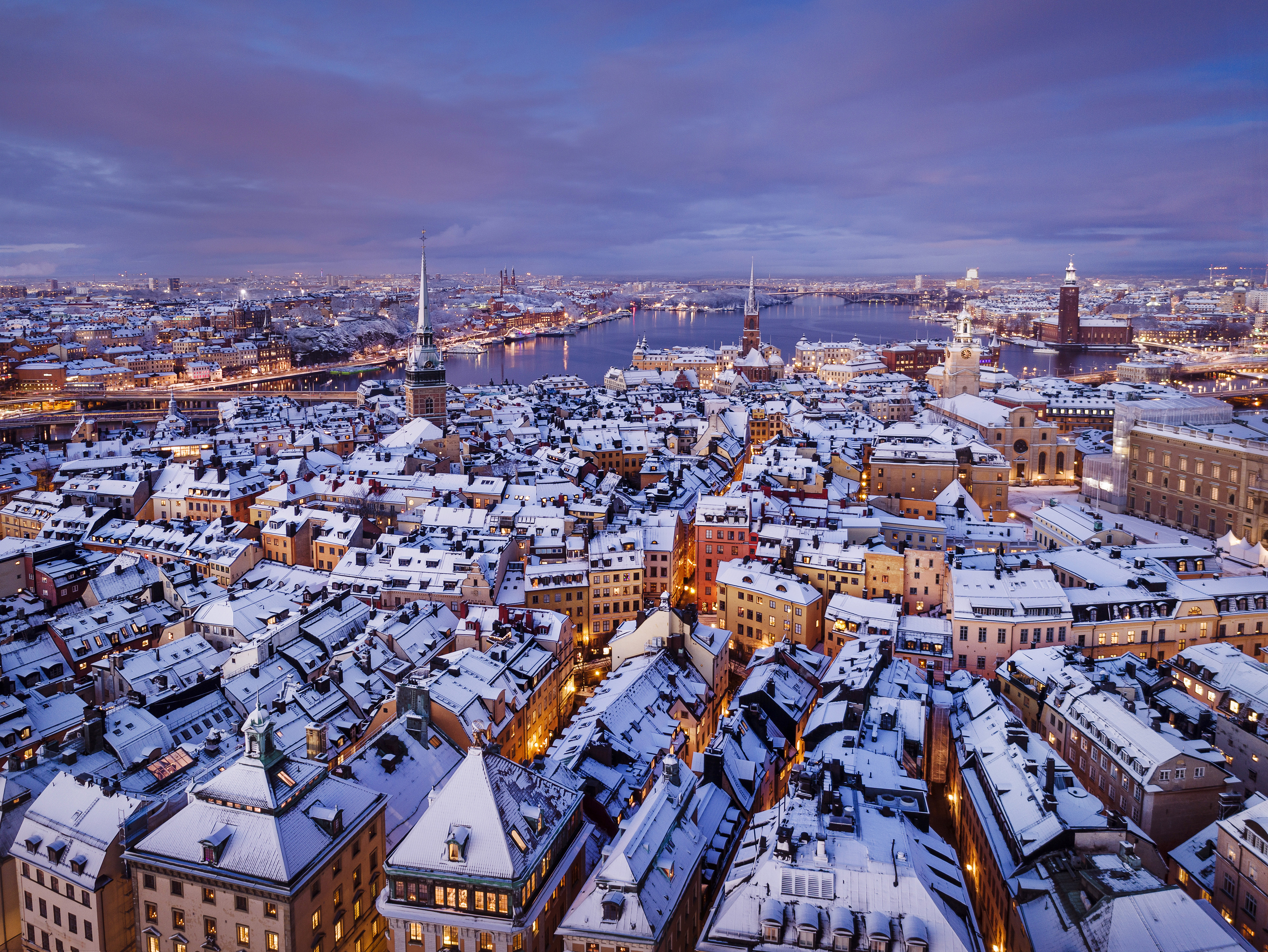 Aerial view of snow-covered Gamla stan in Stockholm at dusk, with colourful historic buildings, church spires and the surrounding city and waterways.