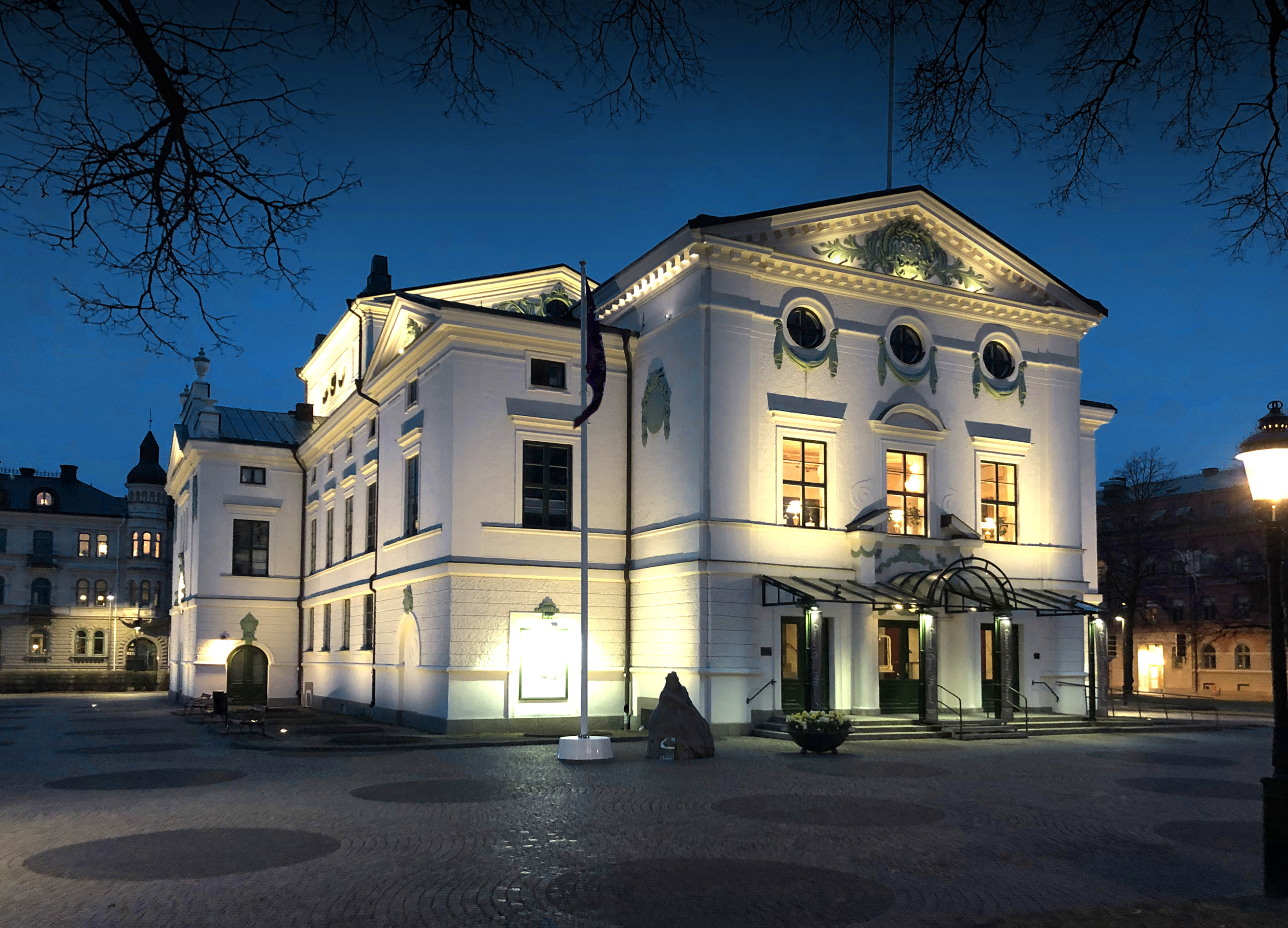 Abendliche Ansicht des beleuchteten Wermland-Opernhauses in Karlstad, Schweden – ein weißes klassisches Theater mit Bogenfenstern und Verzierungen.