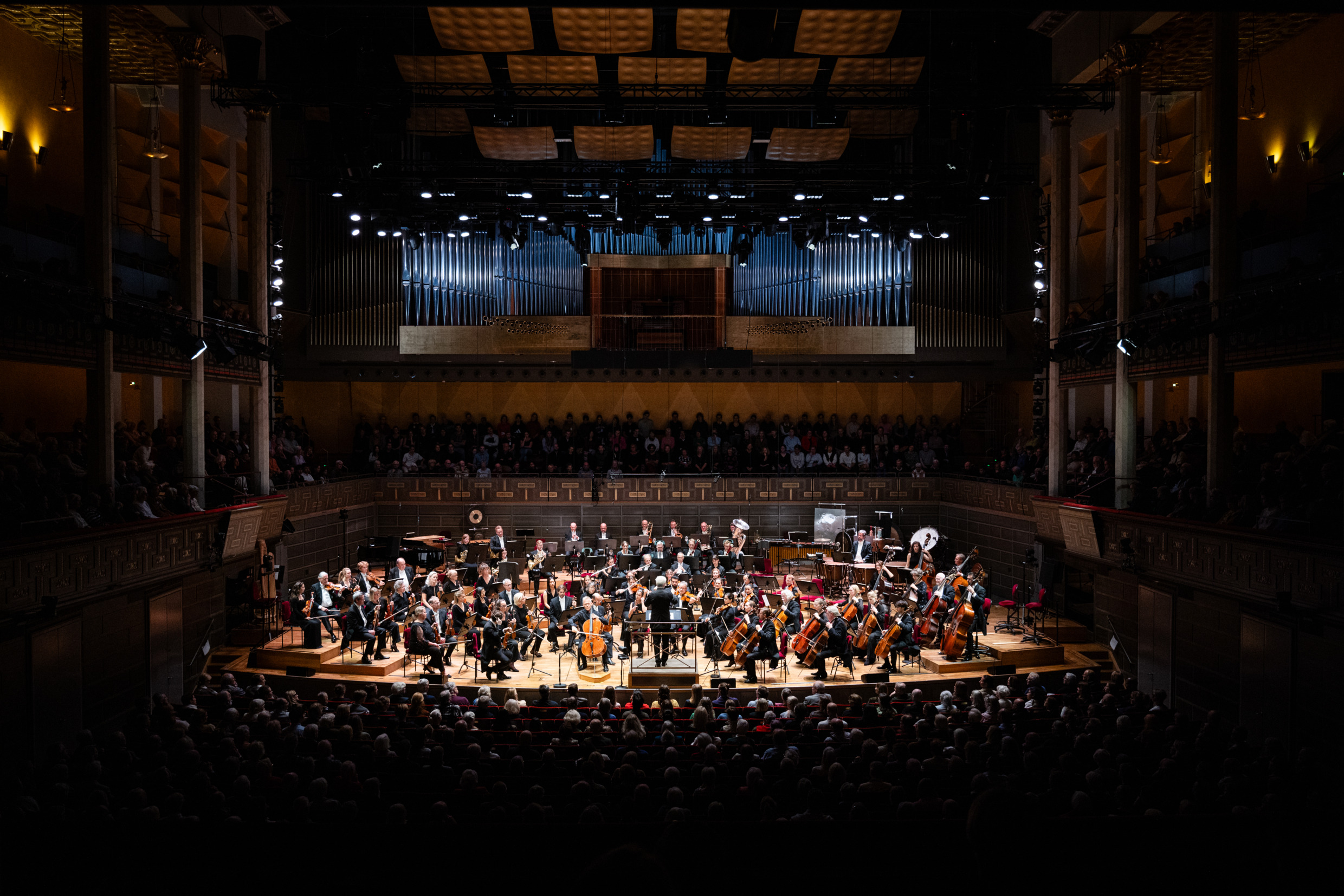 Blick ins Innere der Stockholmer Konzerthalle während einer Live-Orchesteraufführung, mit vollbesetztem Publikum und Musikern auf der Bühne.