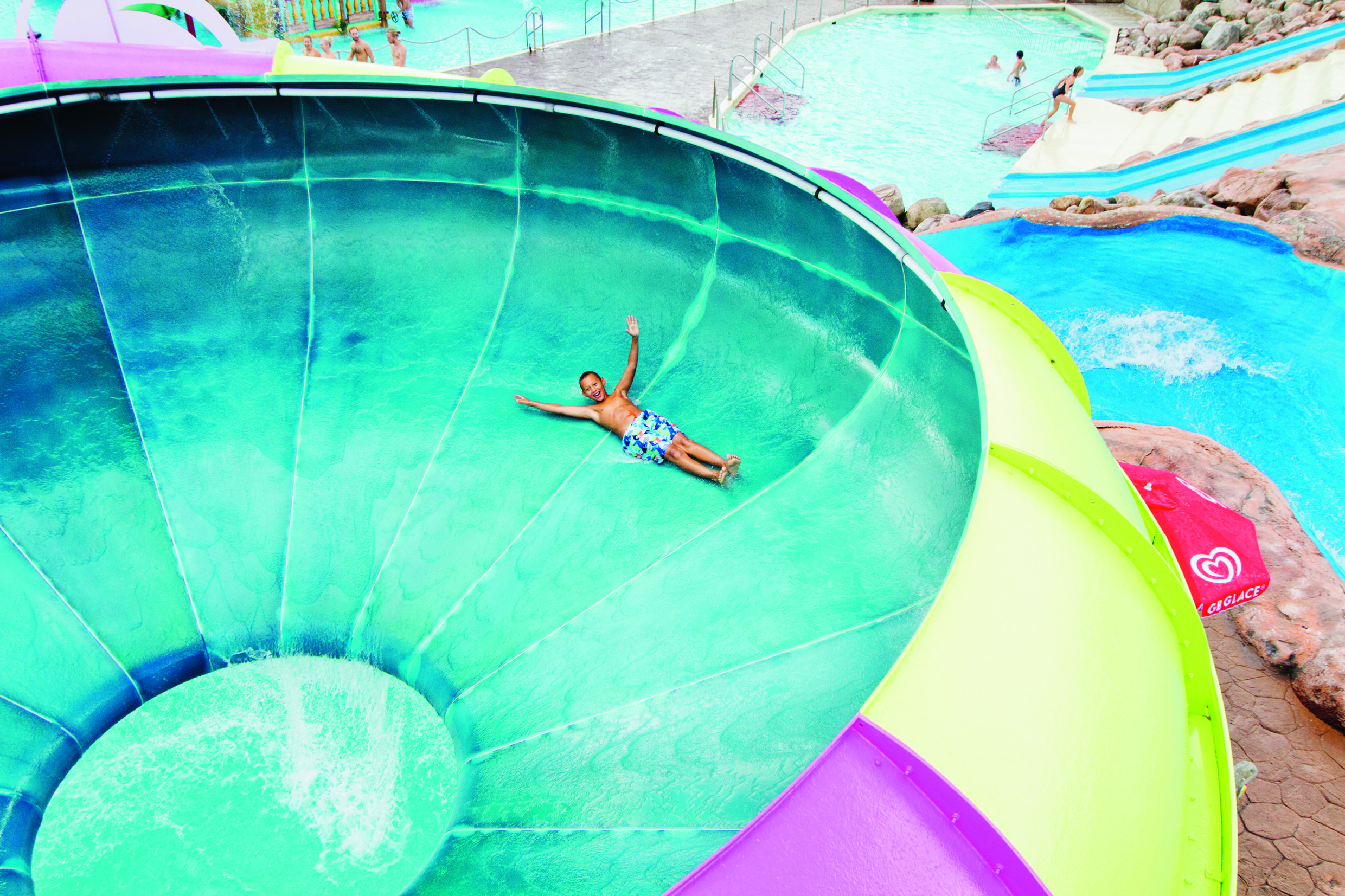 Young boy riding a colorful water slide at Skara Sommarland with the pool area in the background