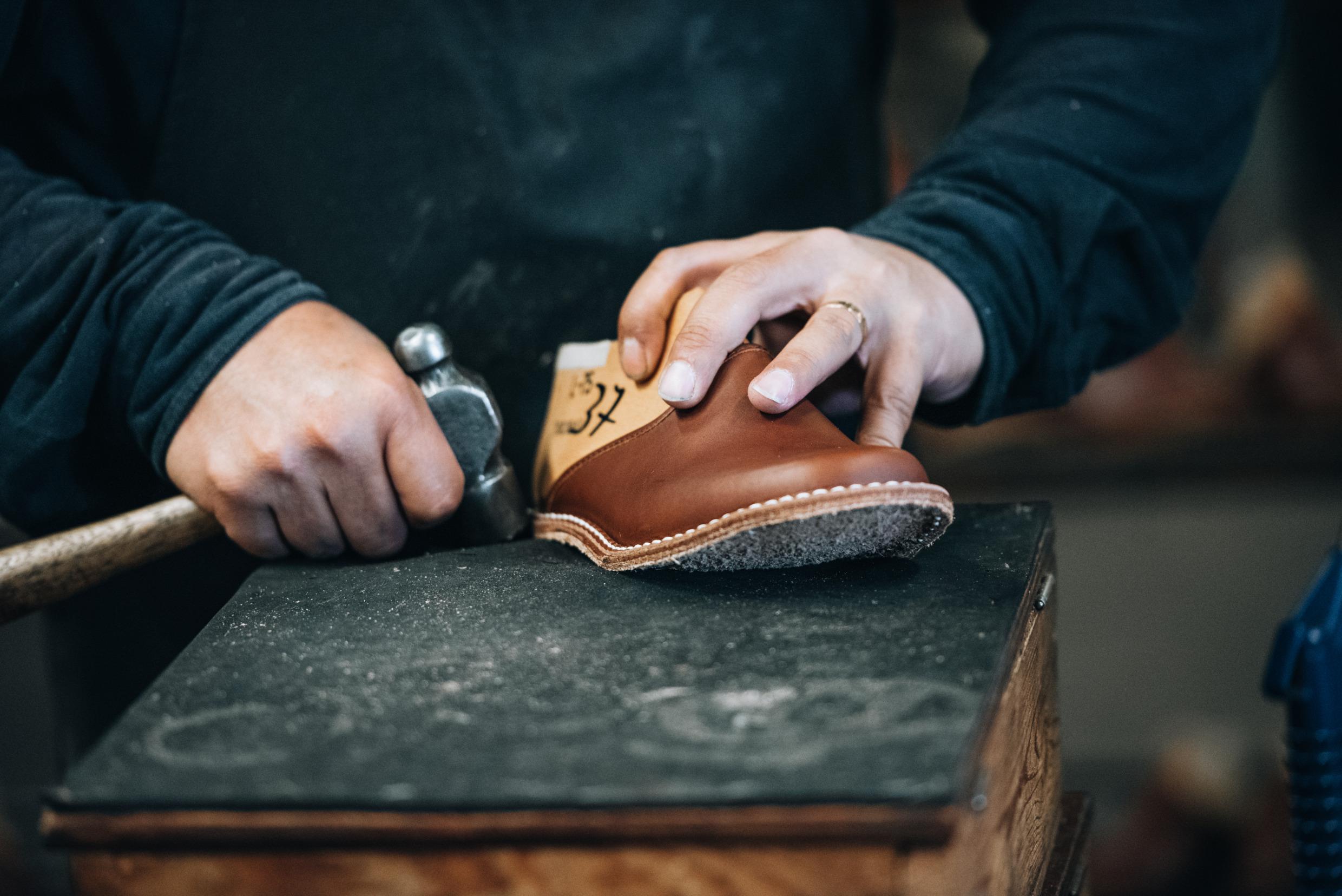 Close-up on hands making slippers at Docksta sko factory. The person is holding a slipper and a hammer in his hands.