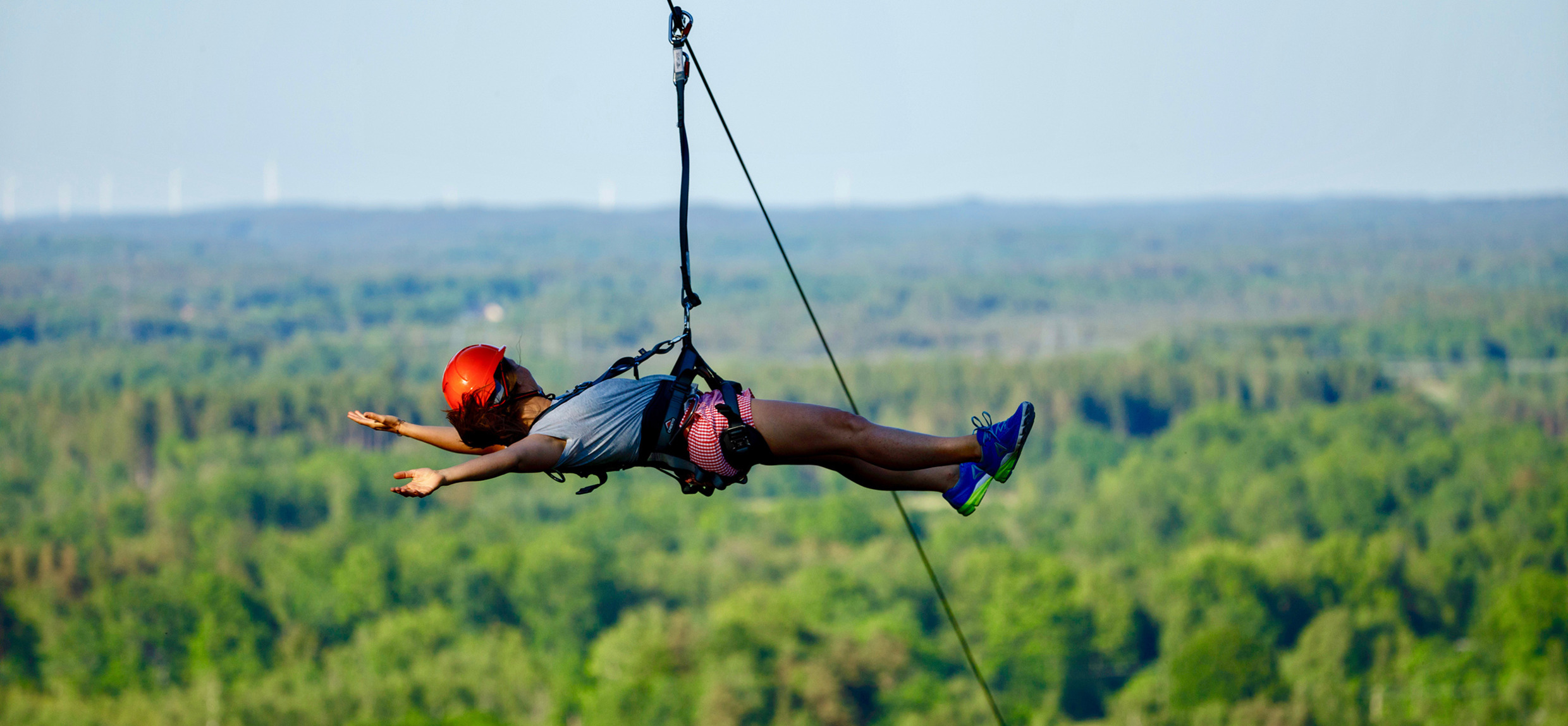A person riding a zipline in a flying position high above the forest at Kungsbygget Adventure Park, wearing a helmet and harness.
