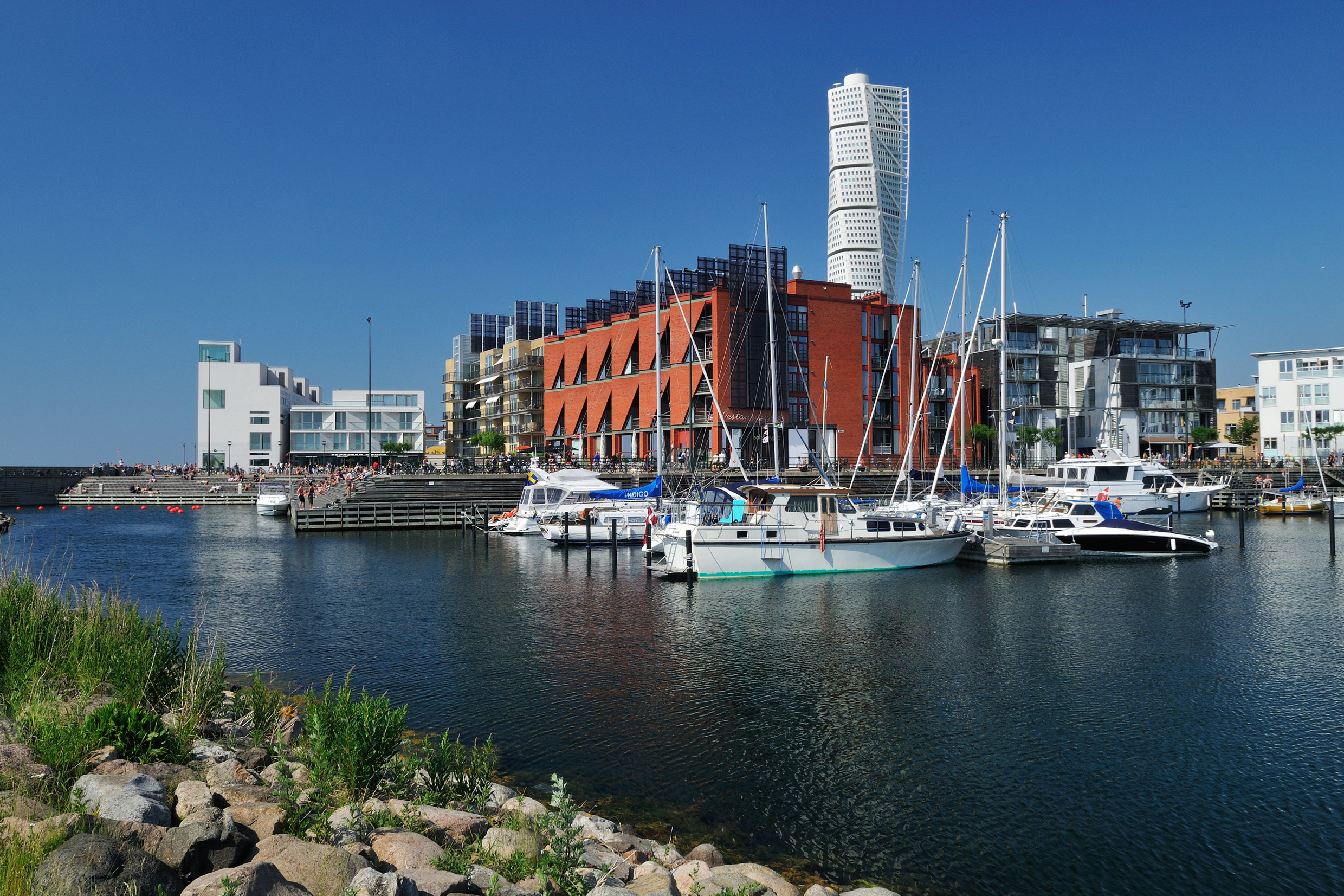 Private boats are moored next to apartment buildings in Malmö's Western Harbour district with the Turning Torso high-rise in the background.
