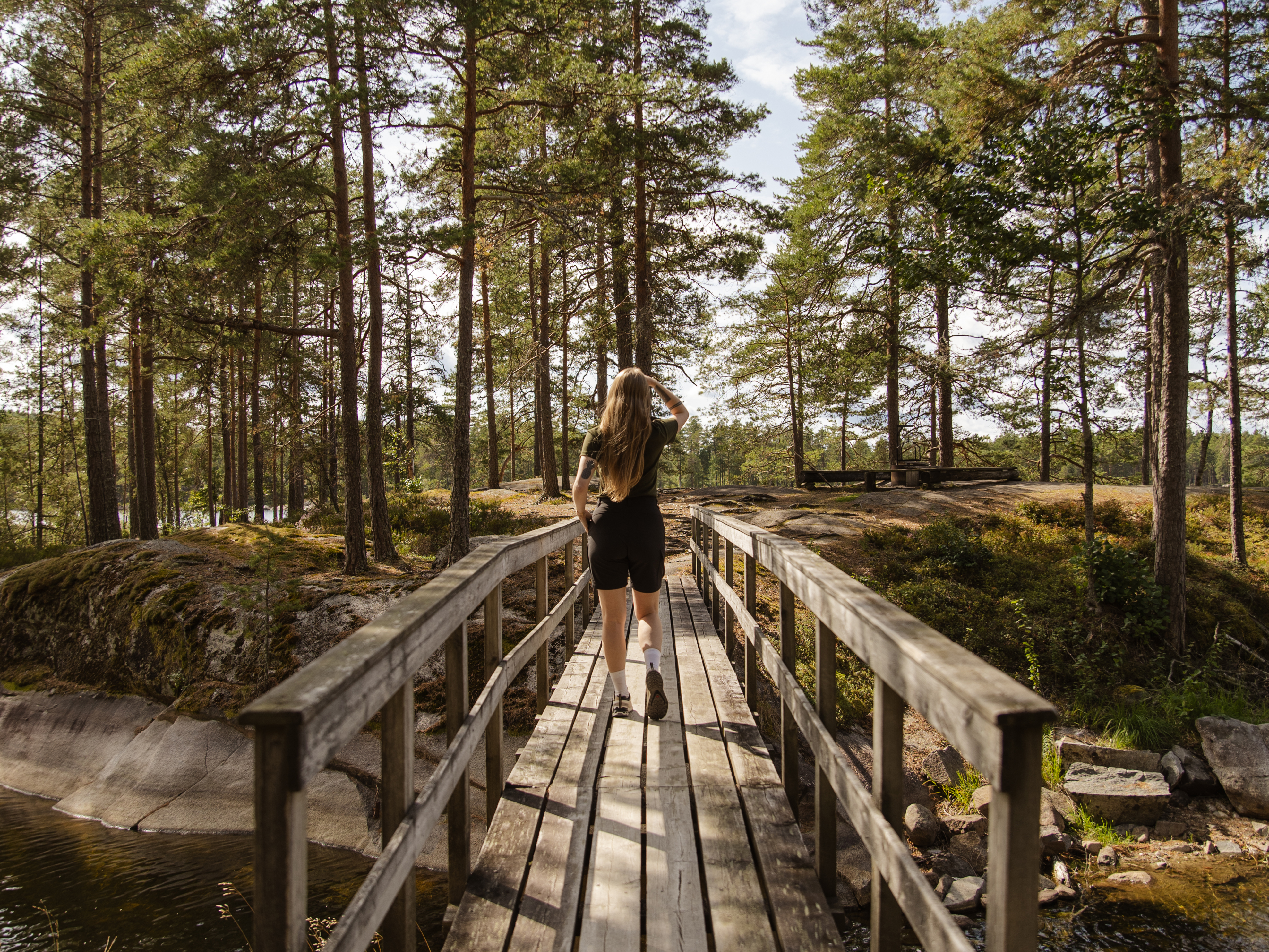 Iemand die over een houten brug over een rivier loopt, omringd door bomen in Glaskogen.