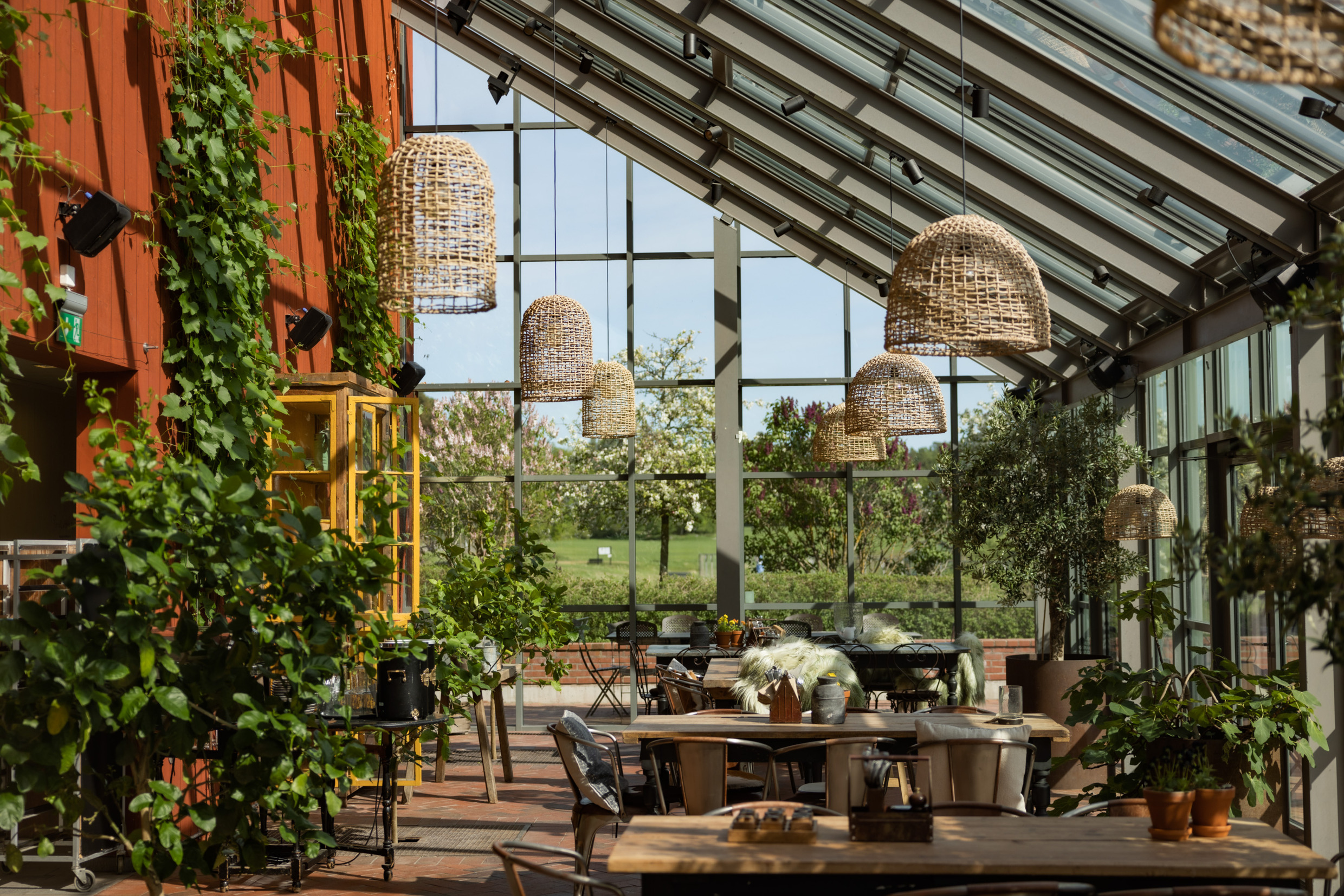 A glass-enclosed patio with chairs, tables, lamps and plants.